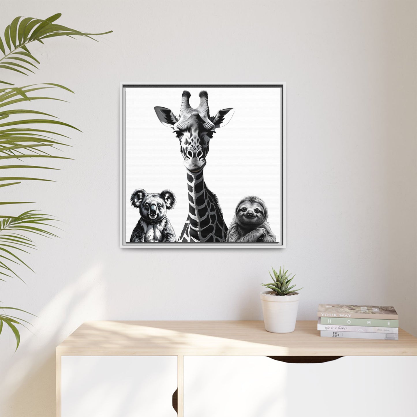 Framed artwork of a giraffe, koala, and sloth on a wall above a desk with plants and books.