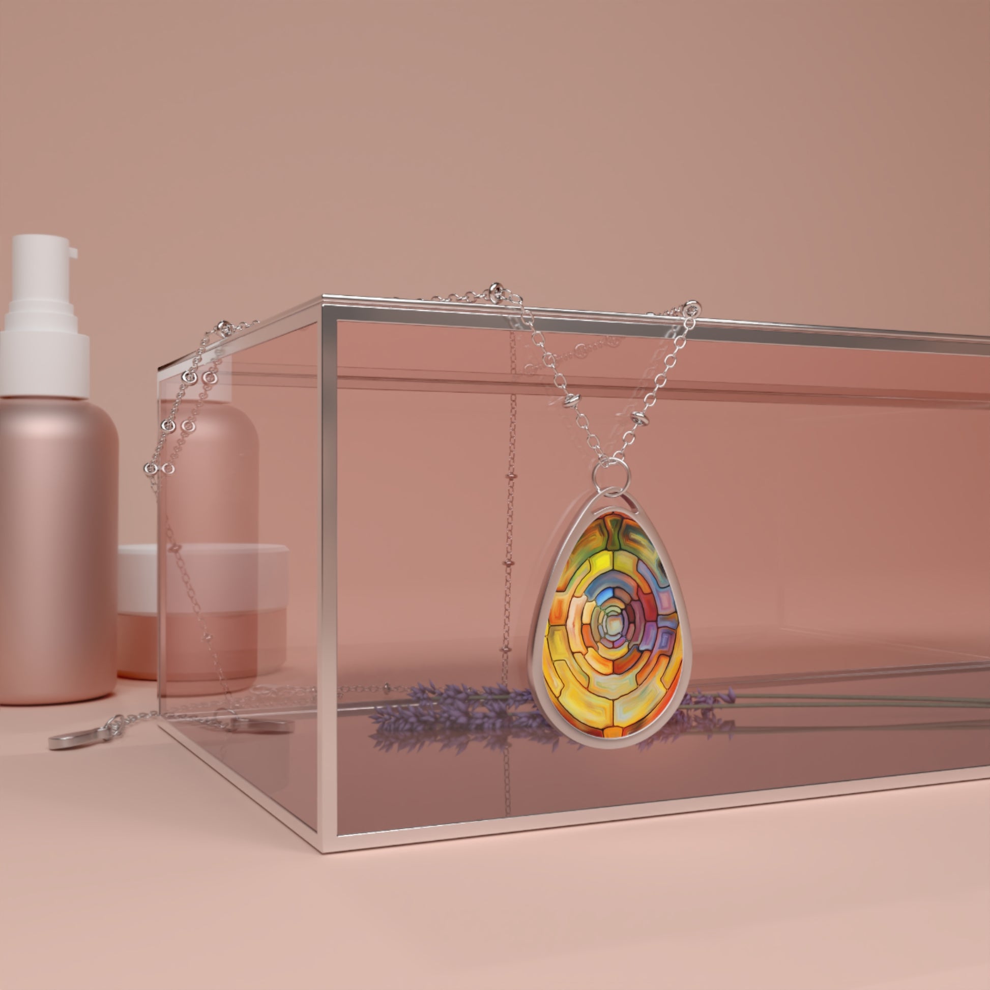 Colorful teardrop-shaped pendant on a chain with a clear box and pink bottles in the background.