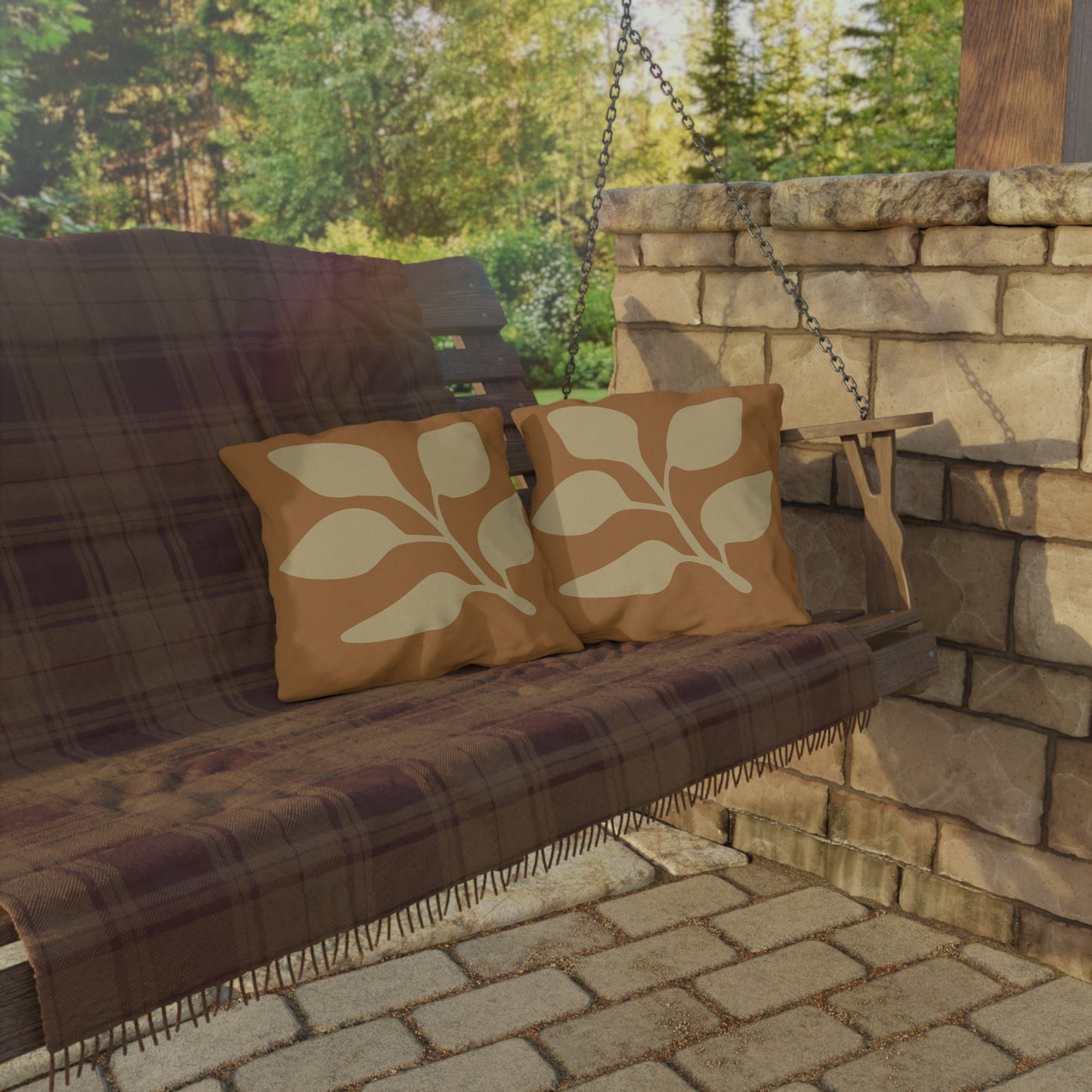 Wooden swing with plaid cover and leaf-patterned pillows on a stone patio.