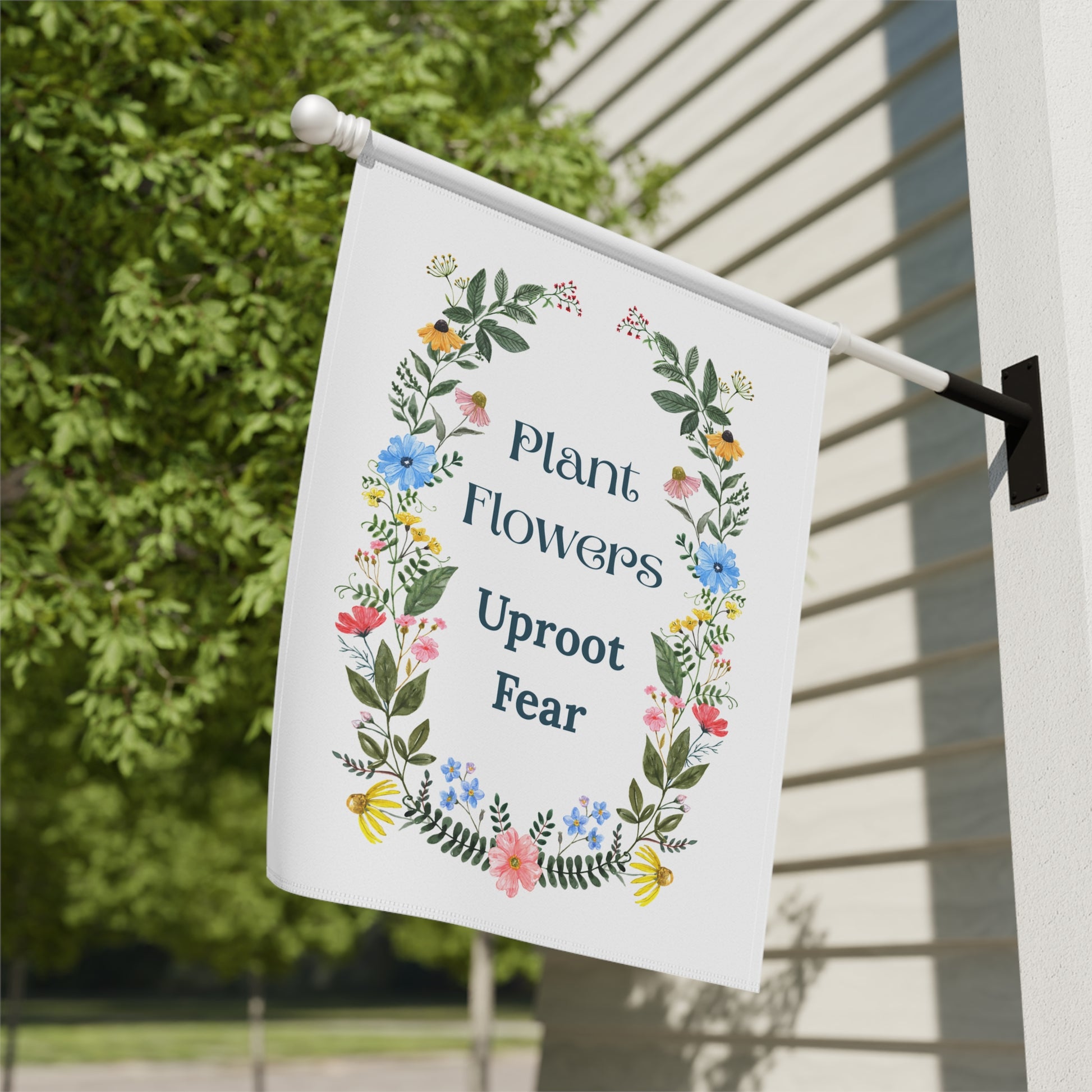 Decorative garden flag with floral design and motivational quote on a pole against a house exterior.