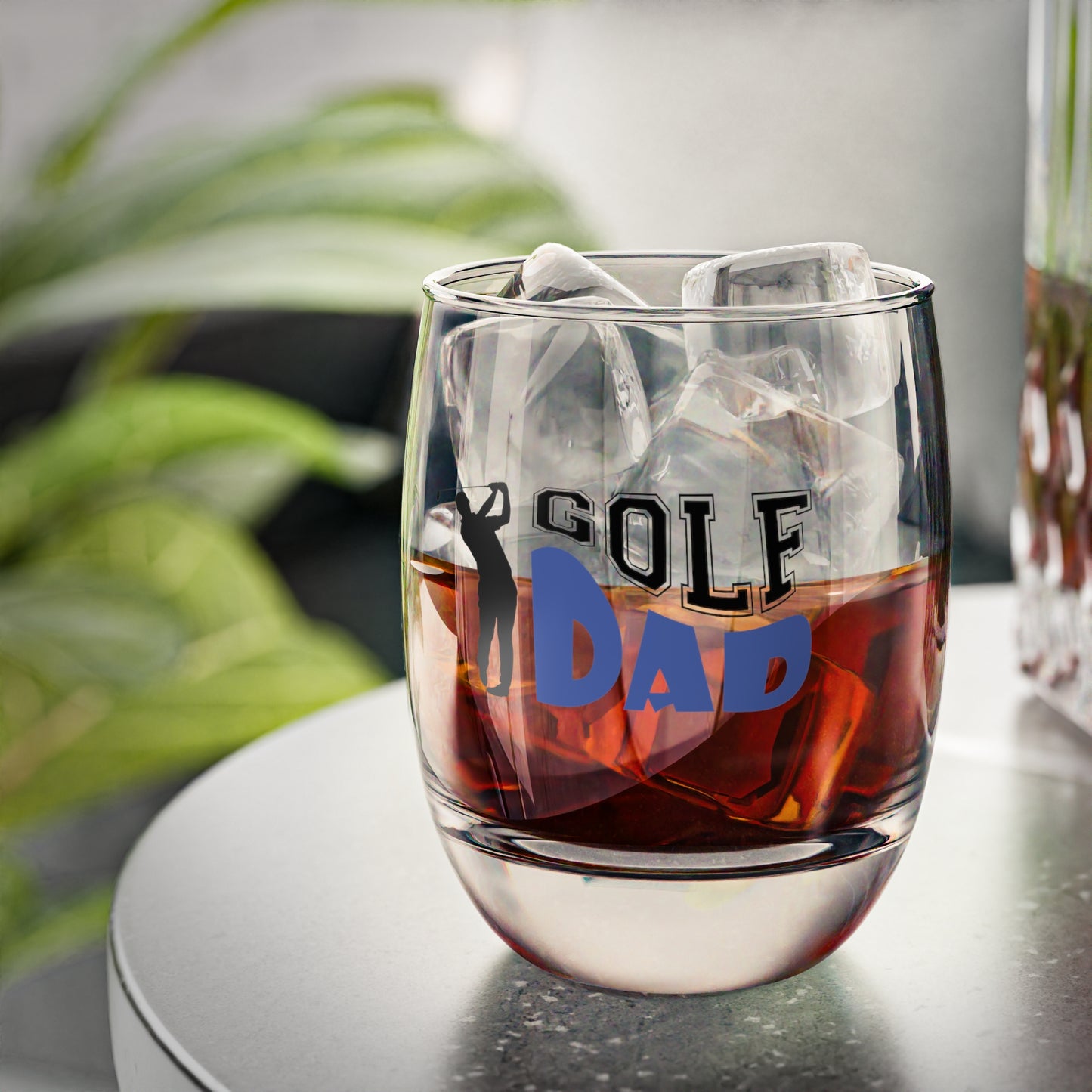 Glass with 'Golf Dad' text filled with a dark liquid on a blurred background
