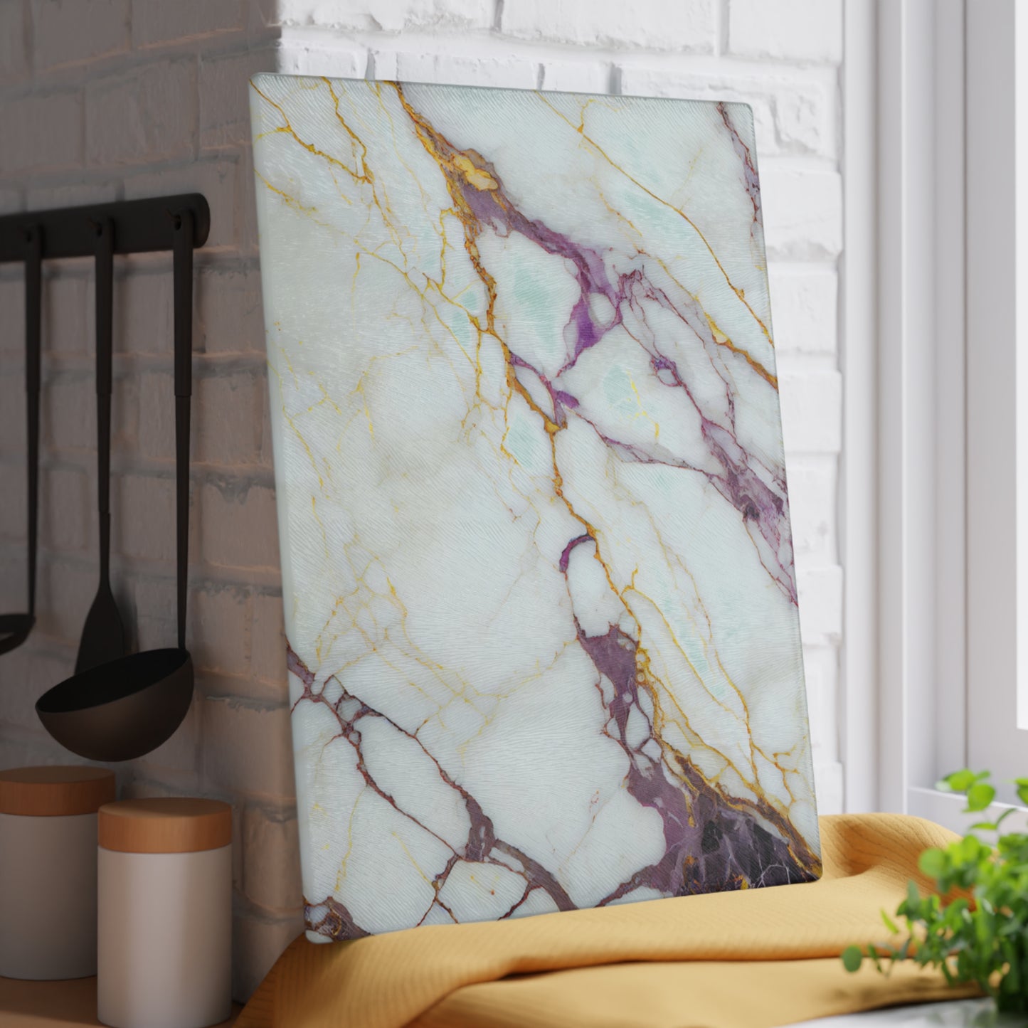 Marble-patterned cutting board on a kitchen counter with utensils and a plant in the background.