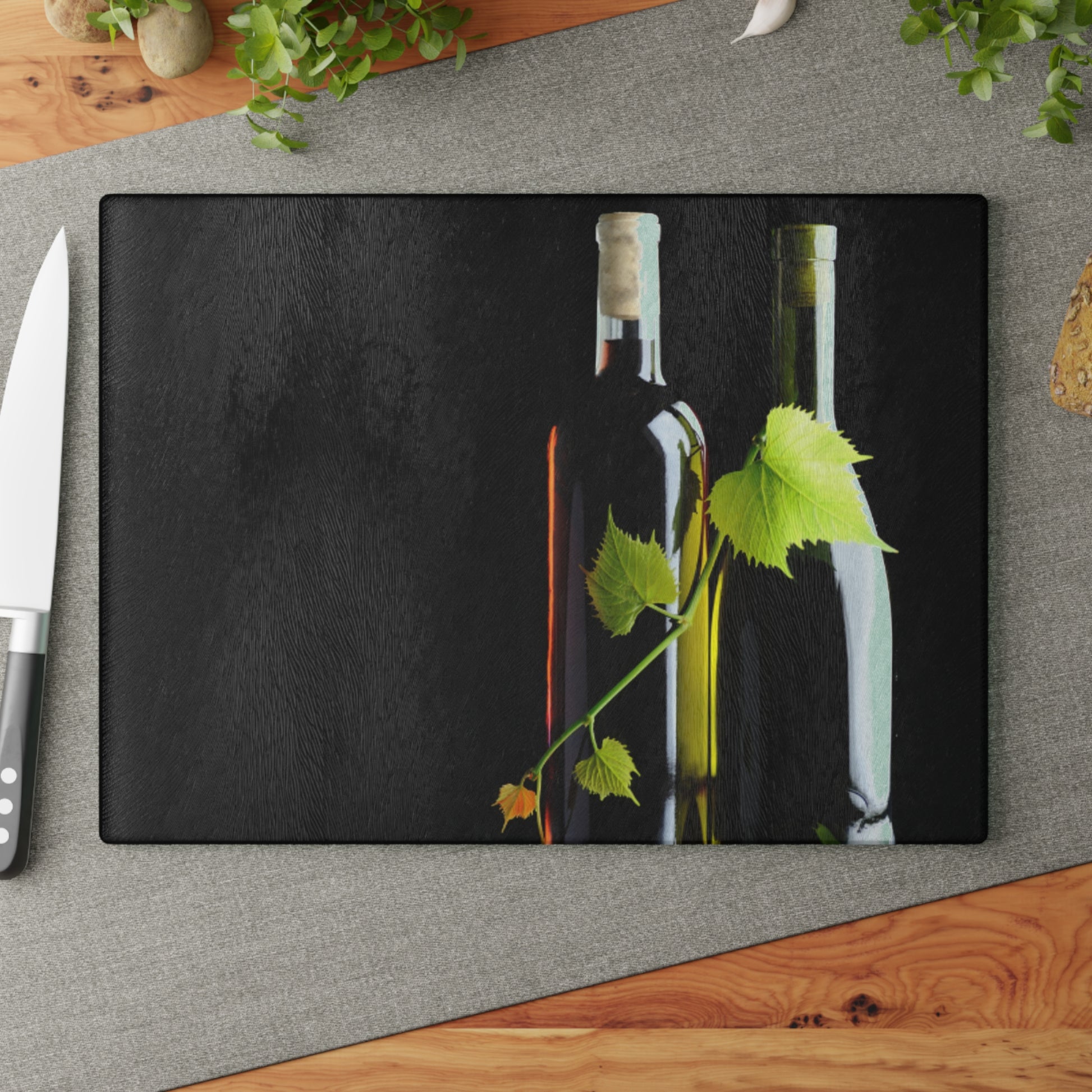Black cutting board with wine bottles and leaves on a gray surface