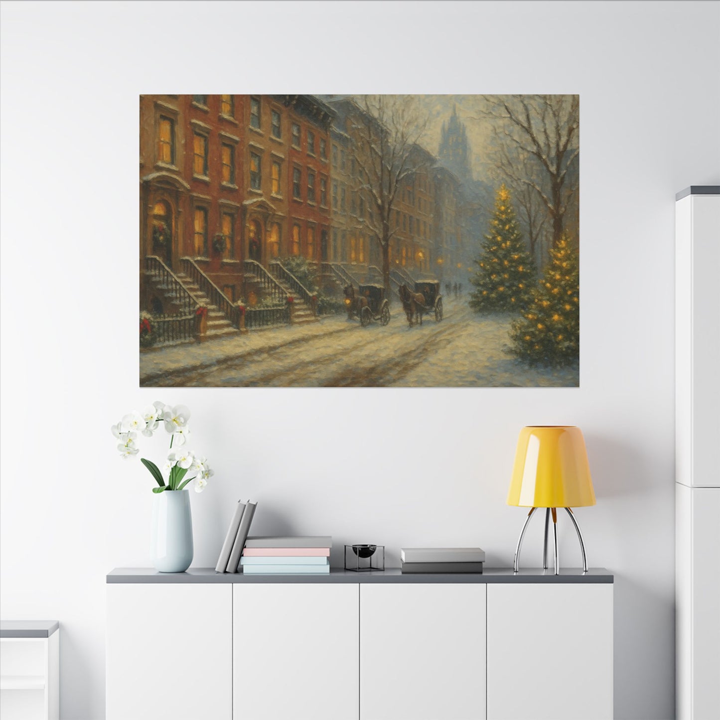 Framed painting of a snowy street scene with a Christmas tree on a wall above a white cabinet.