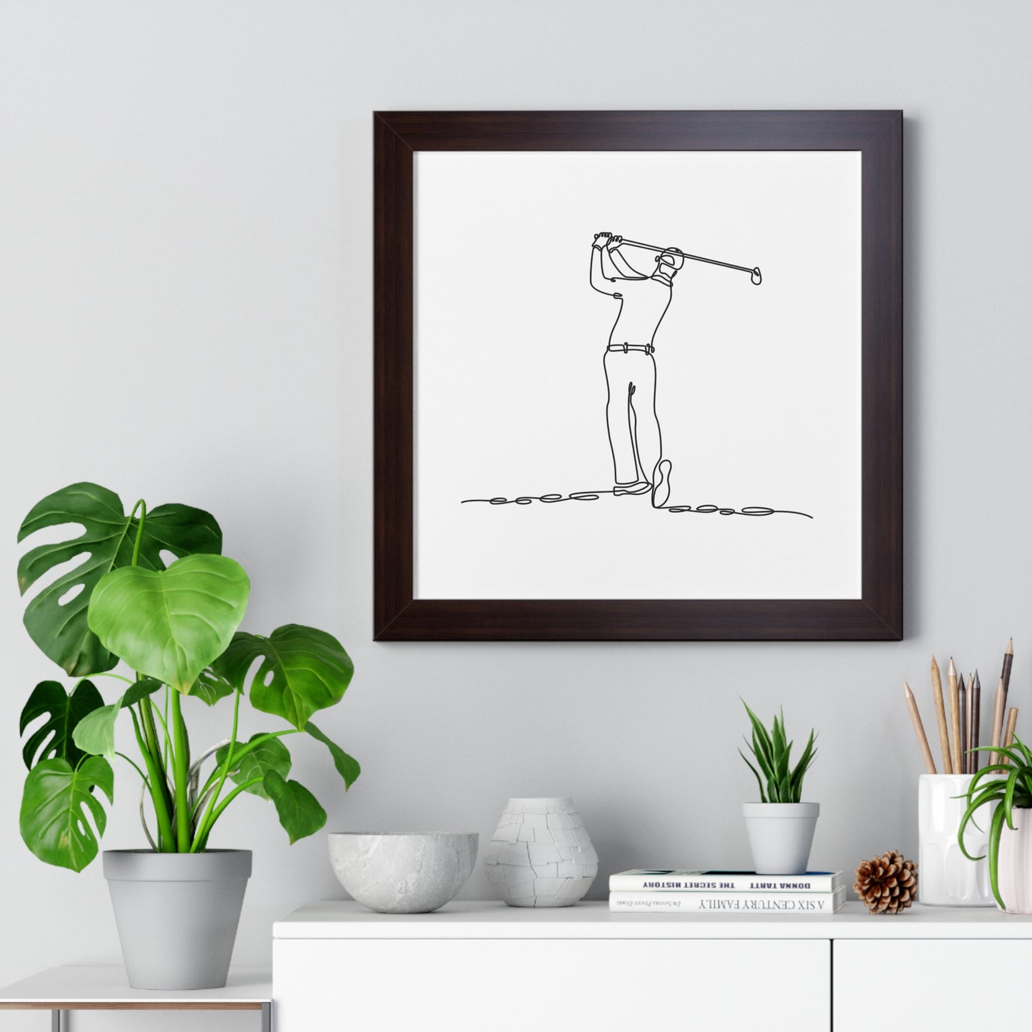 Framed line drawing of a golfer on a wall above a desk with plants and decor.