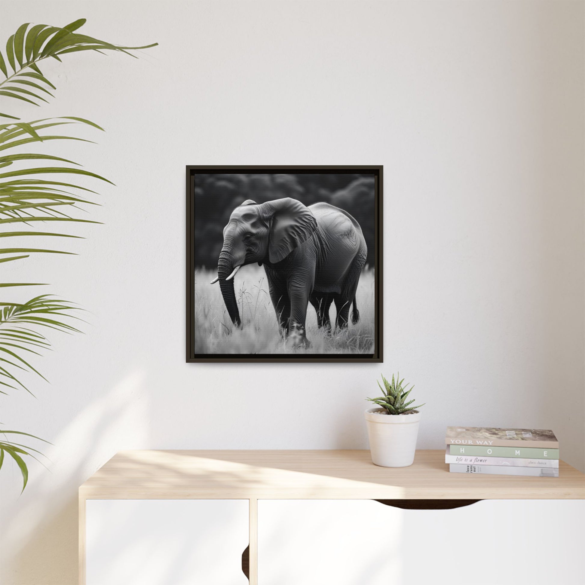 Framed black and white elephant photograph on a wall above a desk with a plant and books.