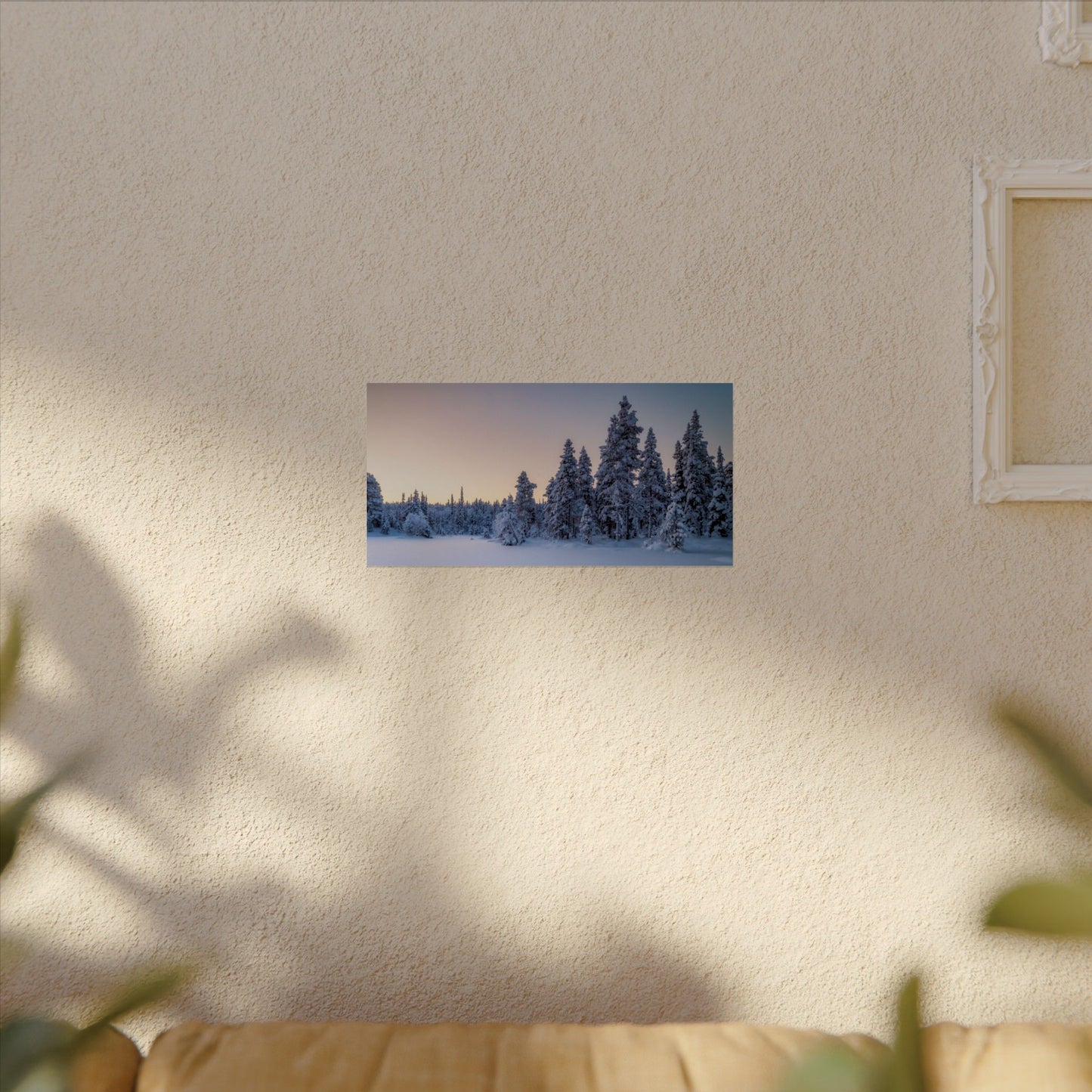 Framed winter landscape print on a wall in a room with a couch and plant.