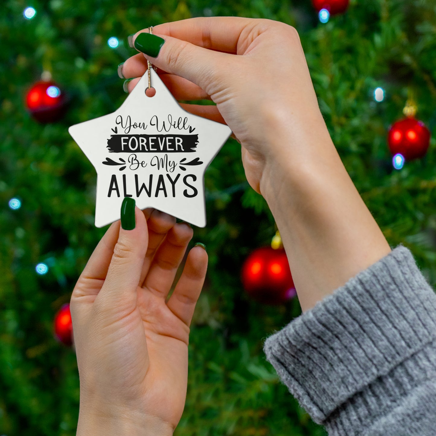 Star-shaped ornament with 'You Will Forever Be My Always' text held by hands against a Christmas tree background.