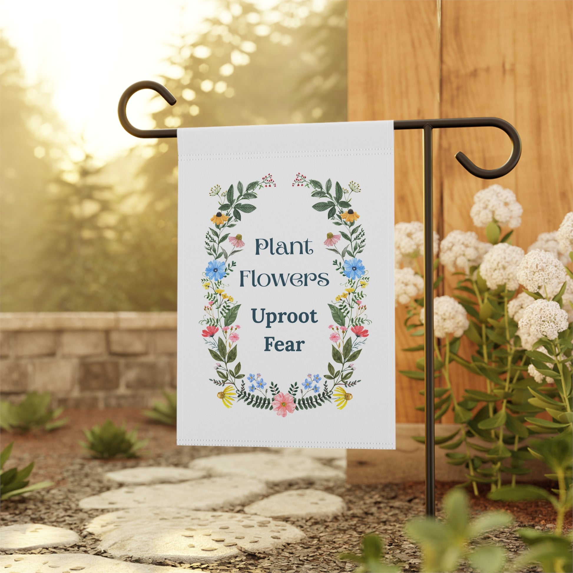 Garden flag with floral design and text 'Plant Flowers Uproot Fear' on a stand outdoors.