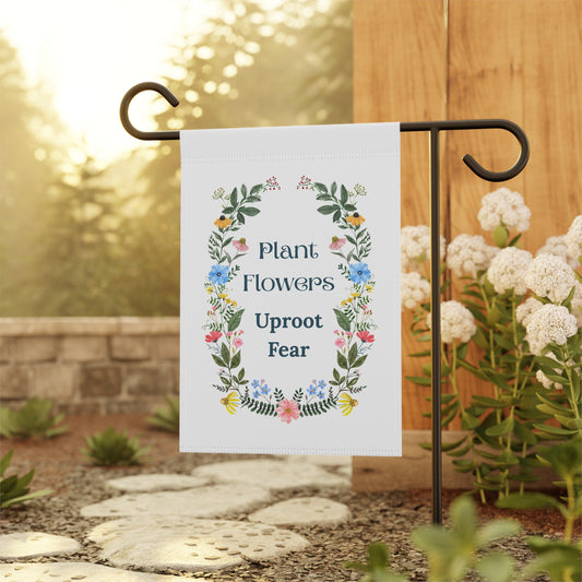 Garden flag with floral design and text 'Plant Flowers Uproot Fear' on a stand outdoors.