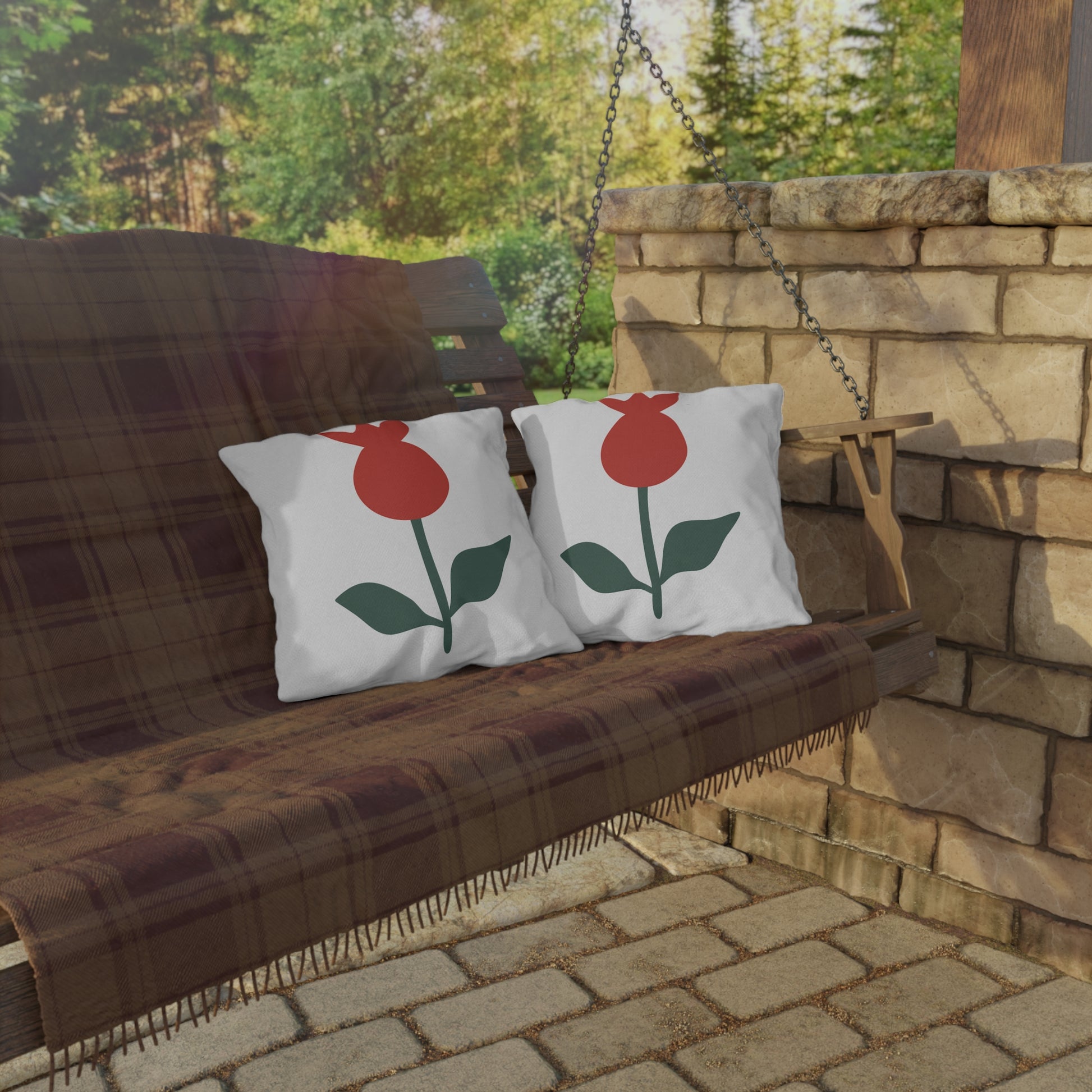 Two pillows with red and green designs on a wooden swing against a stone wall and greenery background.