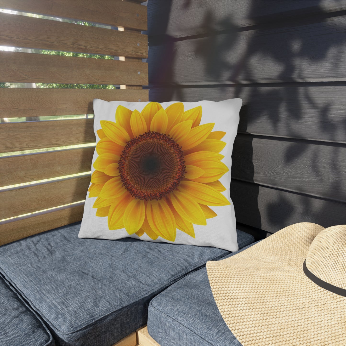 Sunflower pillow on a gray cushioned bench with a straw hat nearby.
