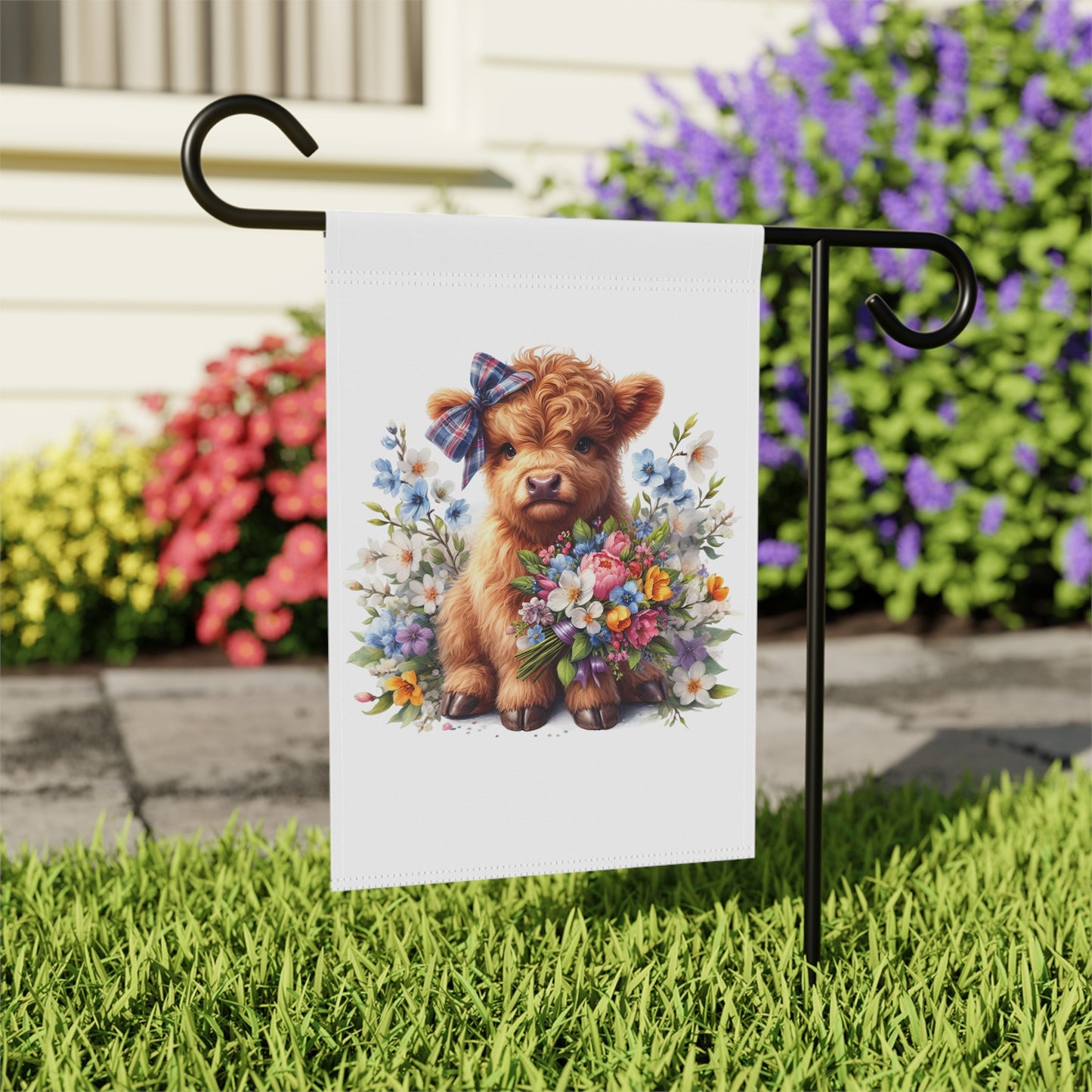 Garden flag with a design of a fluffy brown animal holding flowers, attached to a stand in a garden setting.