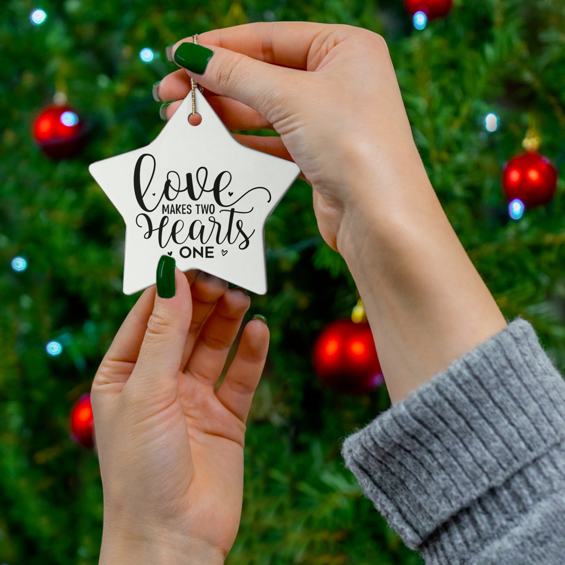 Star-shaped ornament with 'Love makes two hearts one' text held by hands against a Christmas tree background.