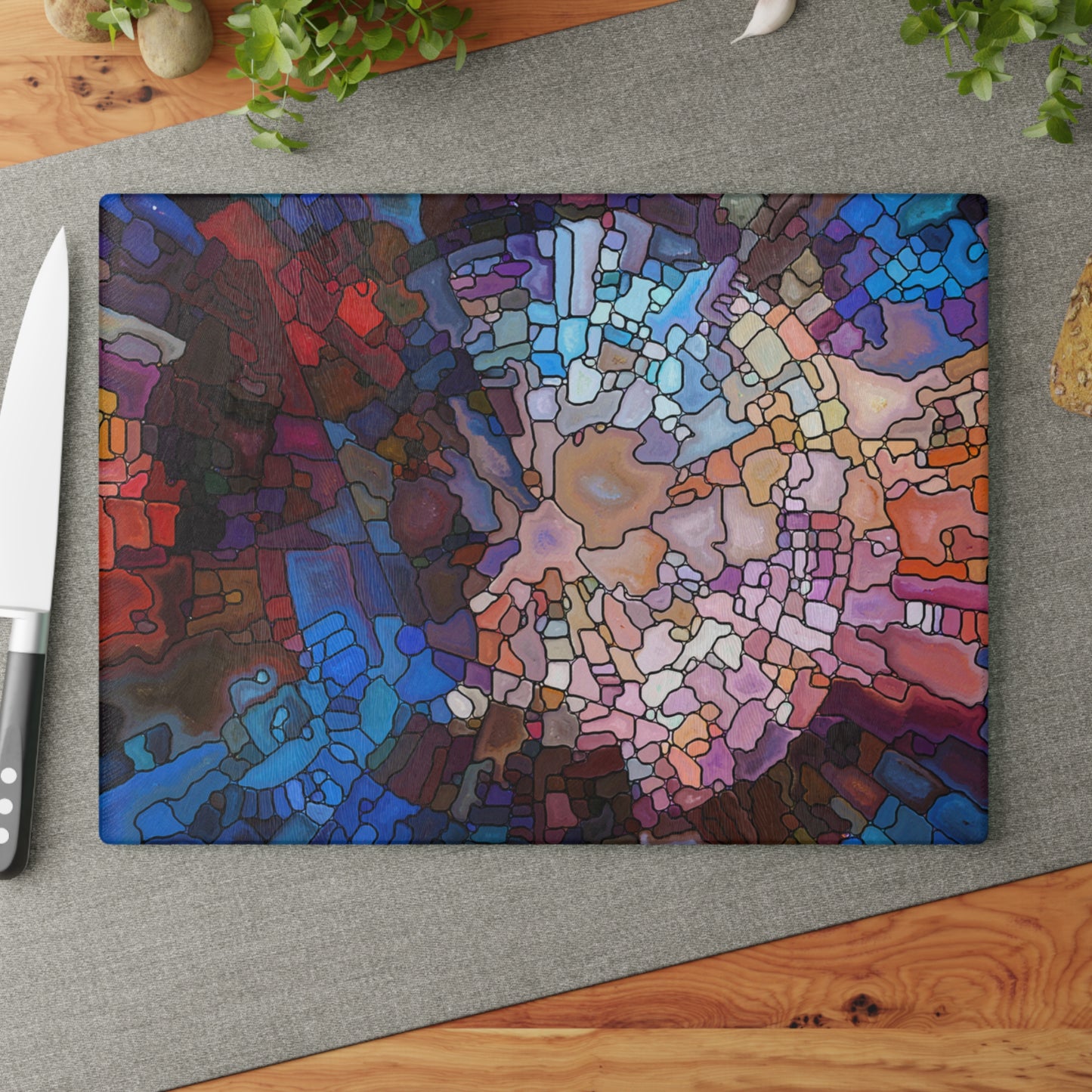 Colorful abstract cutting board on a gray surface with a knife and plant in the background