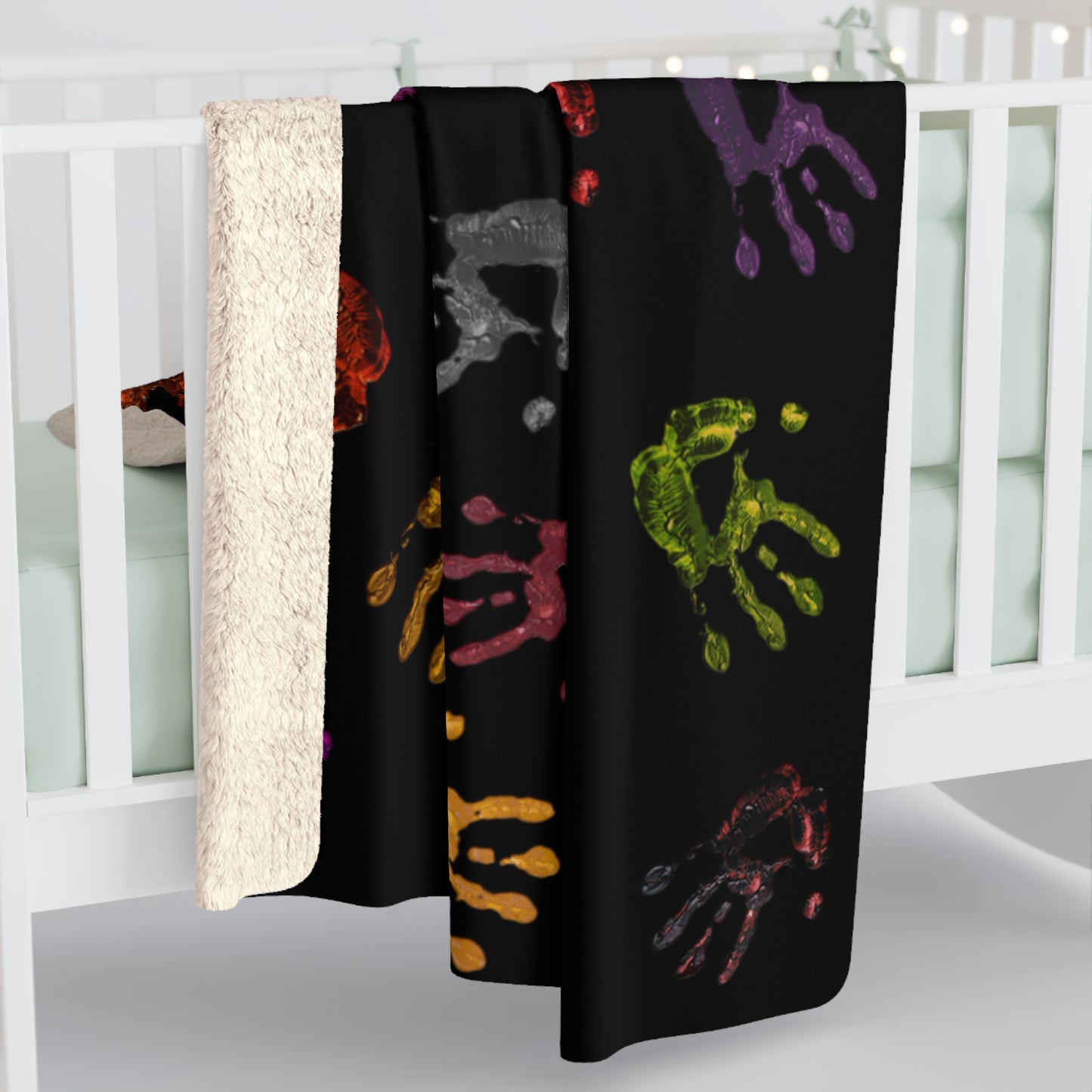Black blanket with colorful handprints draped over a crib.