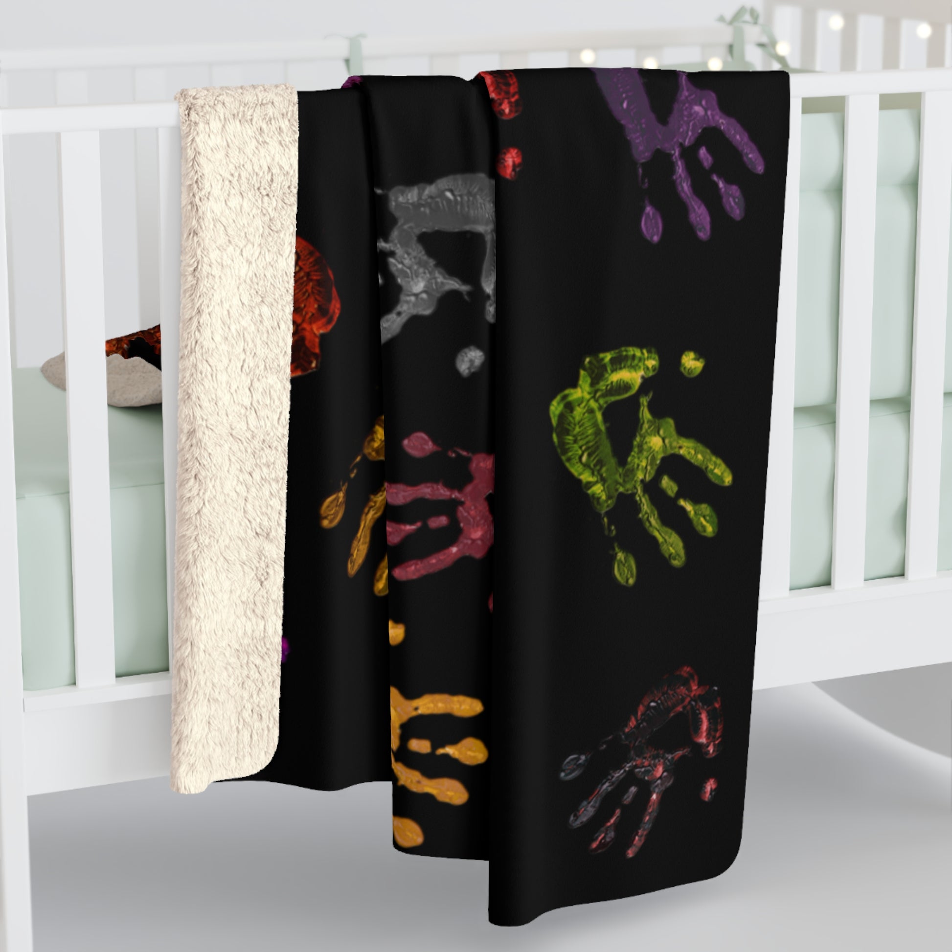 Black blanket with colorful handprints draped over a crib.