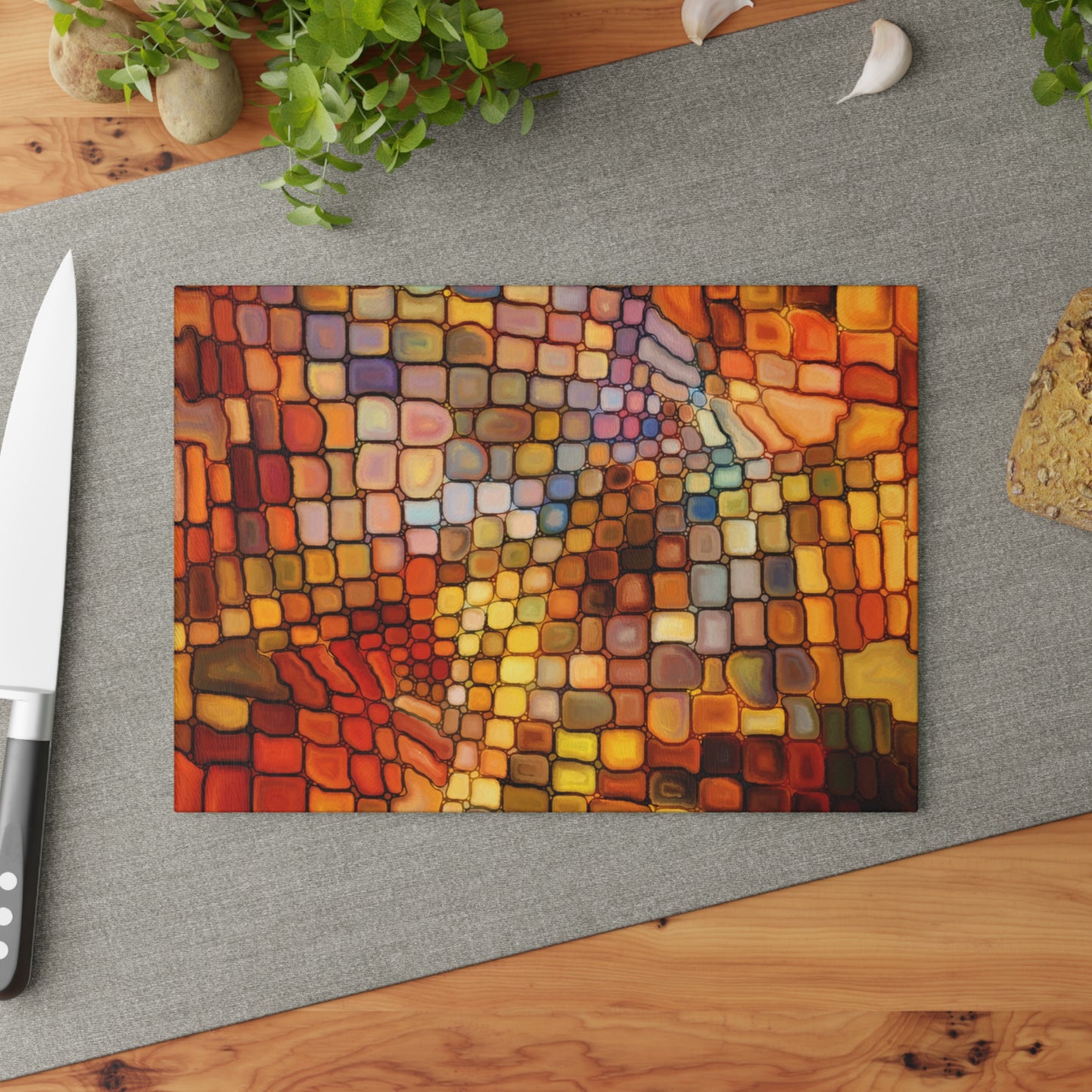 Colorful mosaic cutting board on a gray surface with a knife and plant.