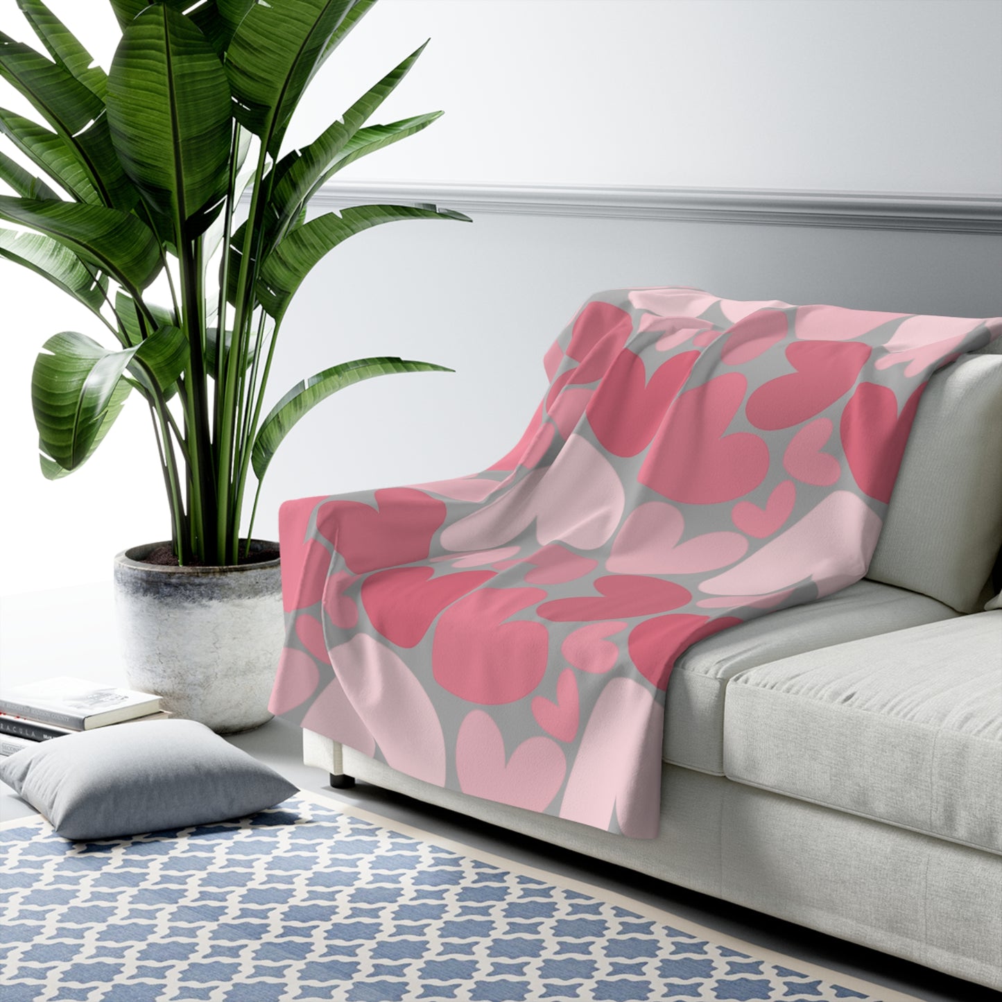 Pink floral blanket on a gray sofa with a plant and rug in the background