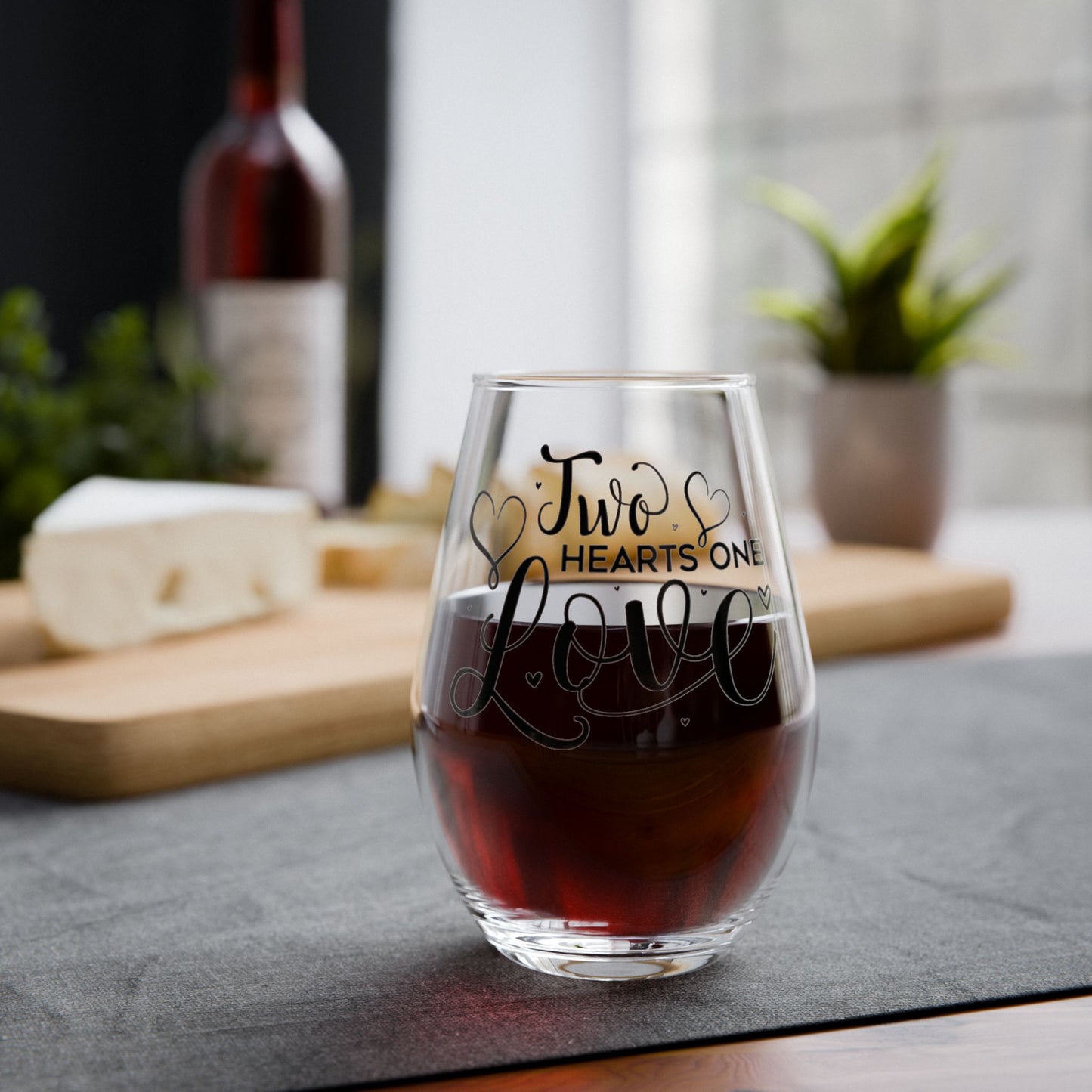 Stemless wine glass with 'Two Hearts One Love' text filled with red wine on a table.