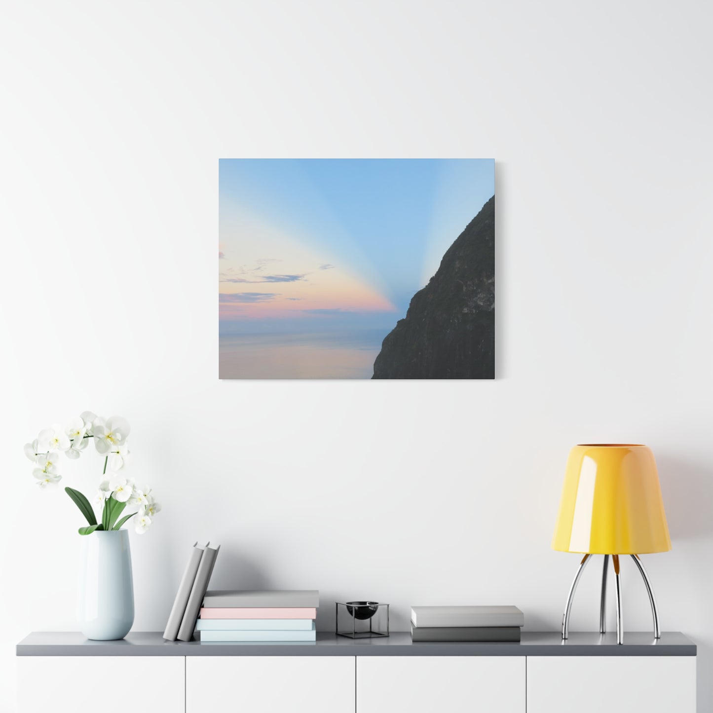 Canvas print of a sunset over a cliff hanging on a wall above a shelf with decor items.