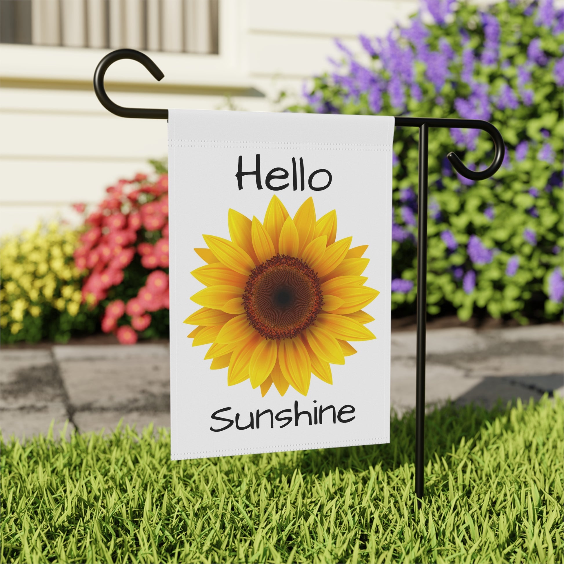 Garden flag with sunflower and 'Hello Sunshine' text on grass with flowers in the background