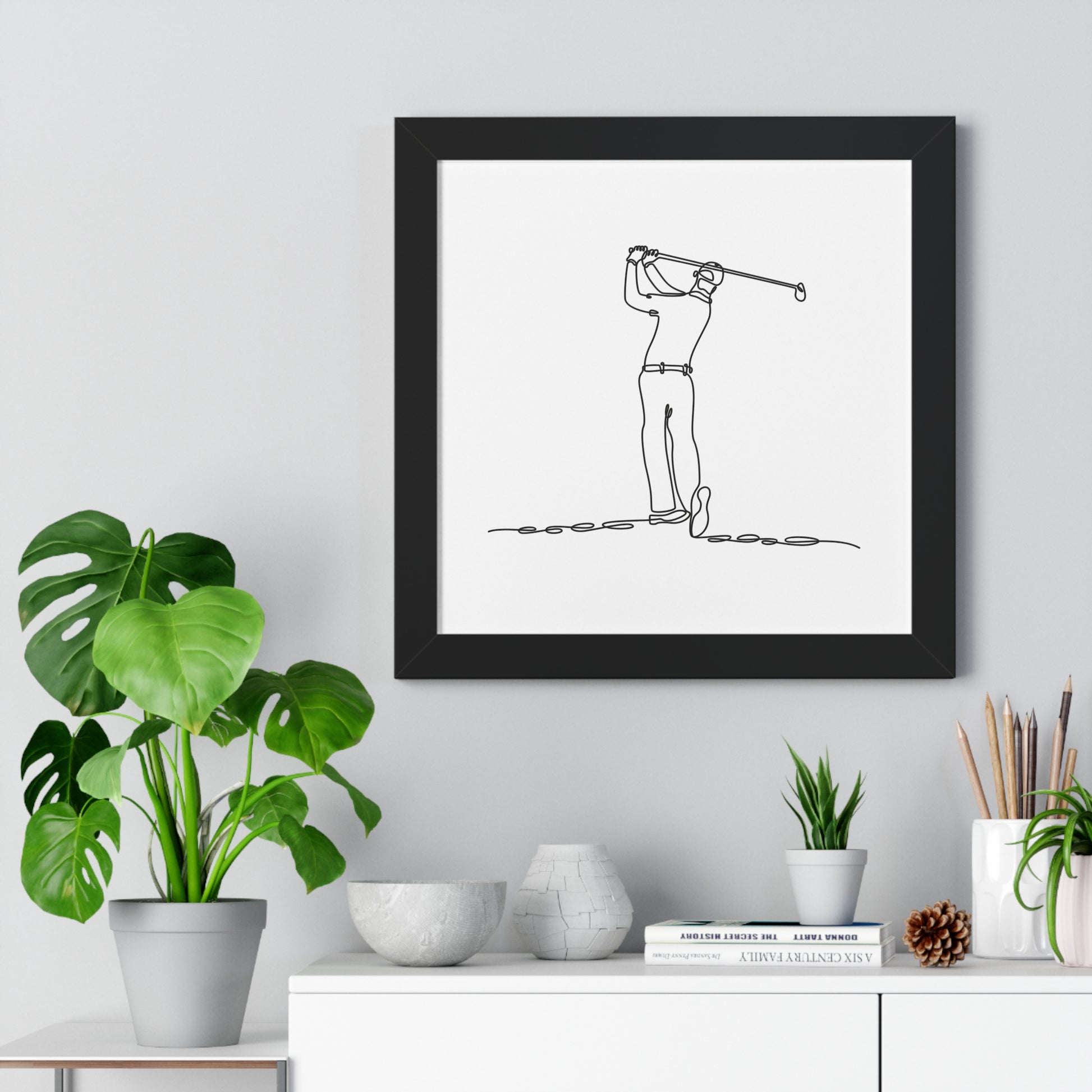 Framed line drawing of a golfer on a wall above a desk with plants and decor.