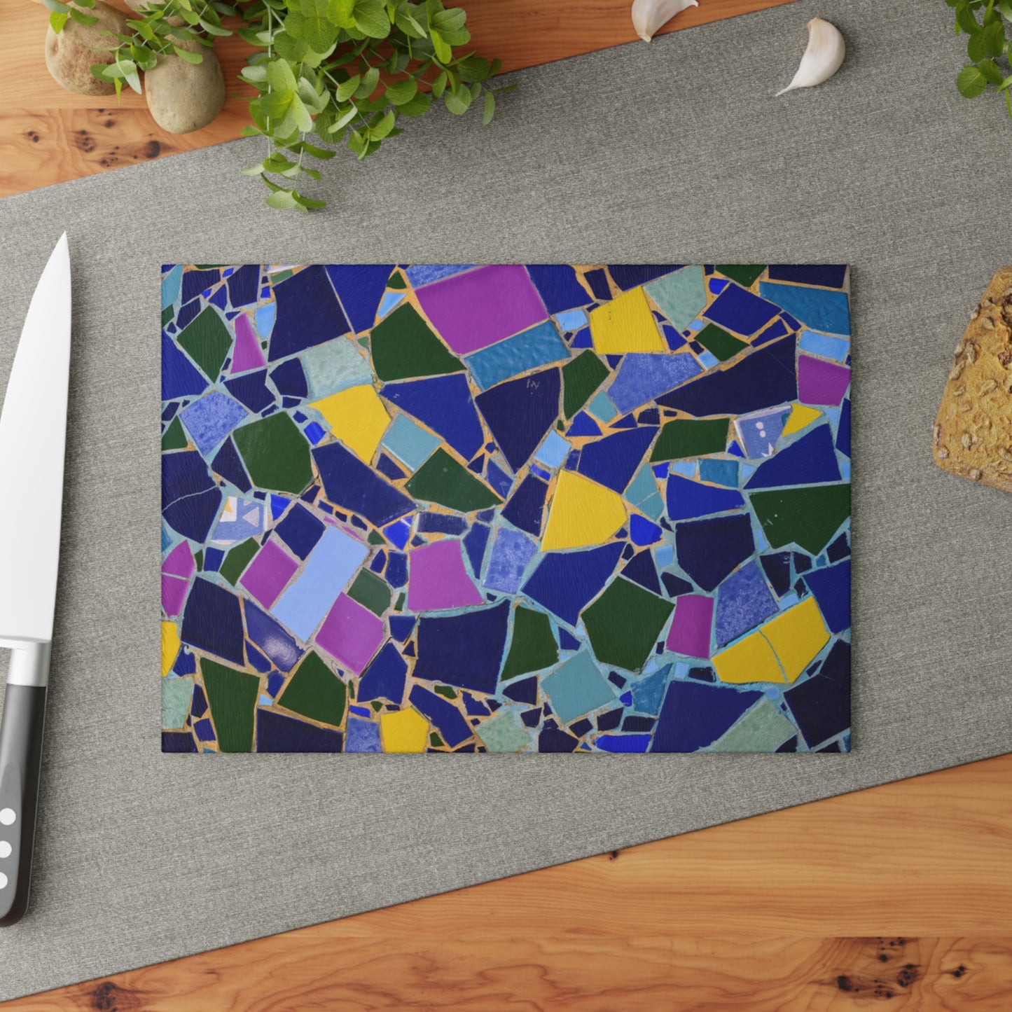 Colorful mosaic cutting board on a gray surface with a knife and plant in the background.