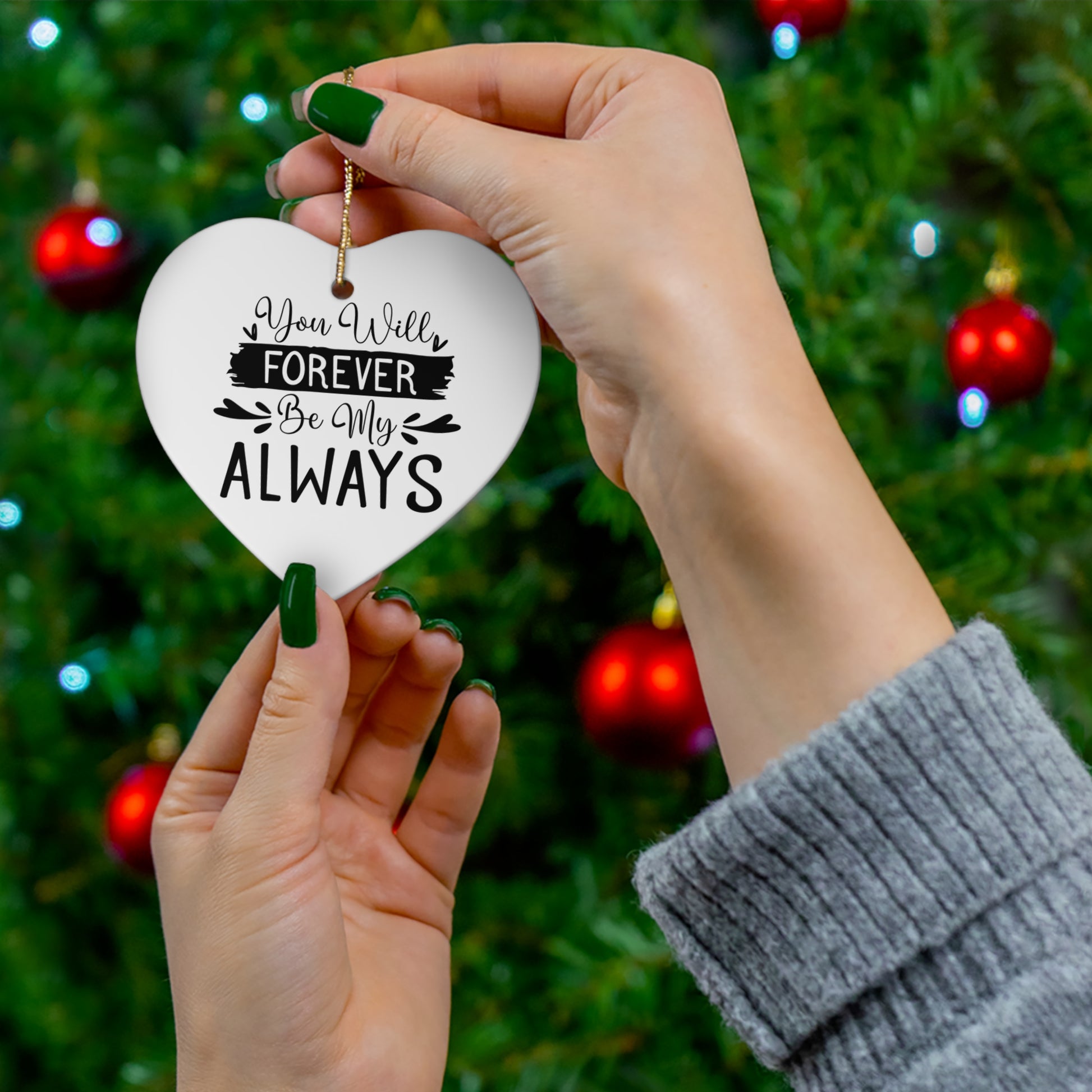 Heart-shaped ornament with romantic text held by hands against a Christmas tree background