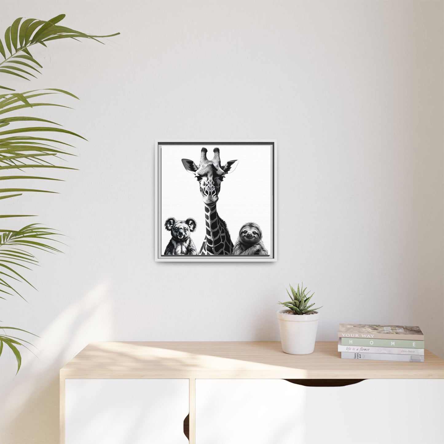 Framed artwork of a giraffe and sloths on a wall above a desk with a plant.