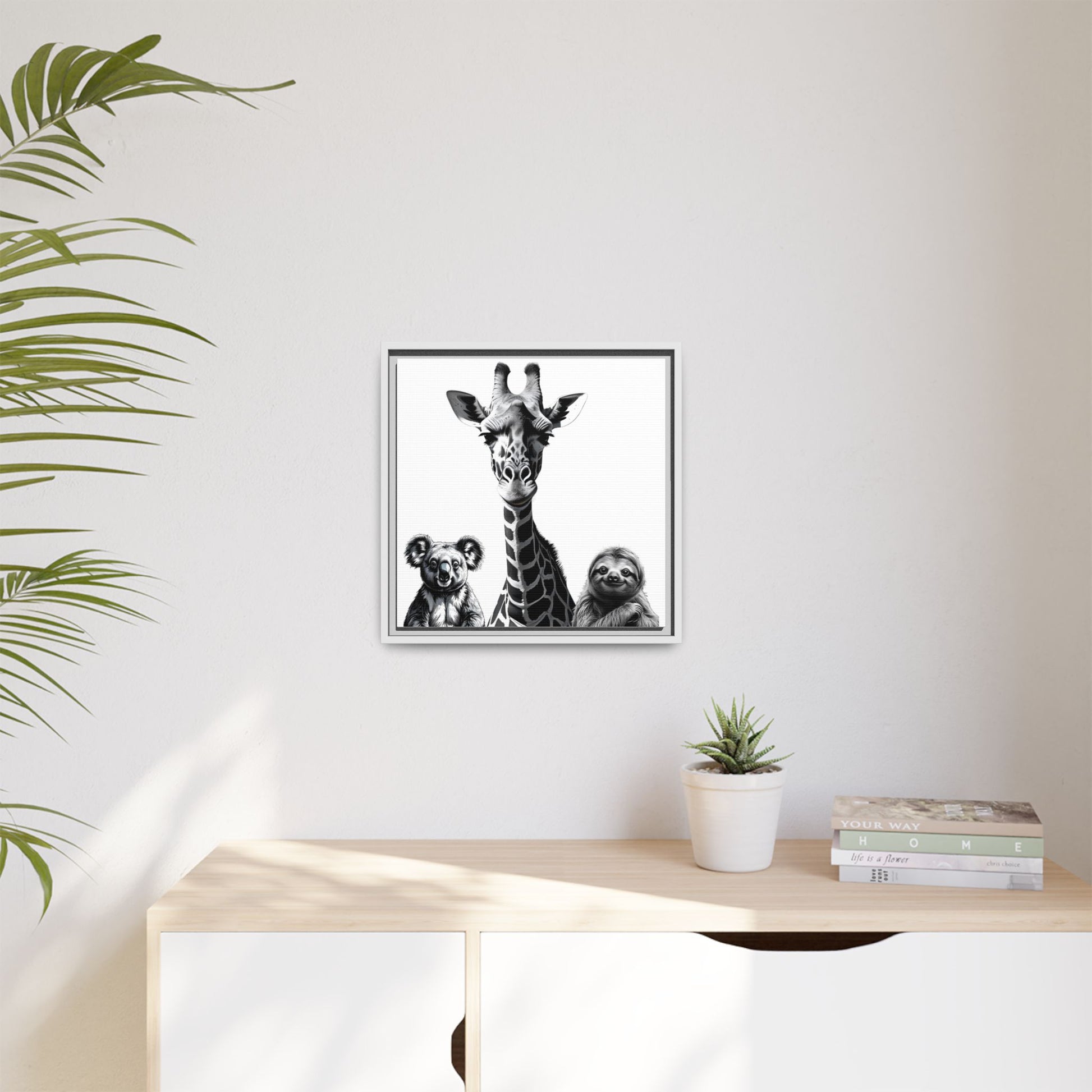 Framed artwork of a giraffe and sloths on a wall above a desk with a plant.