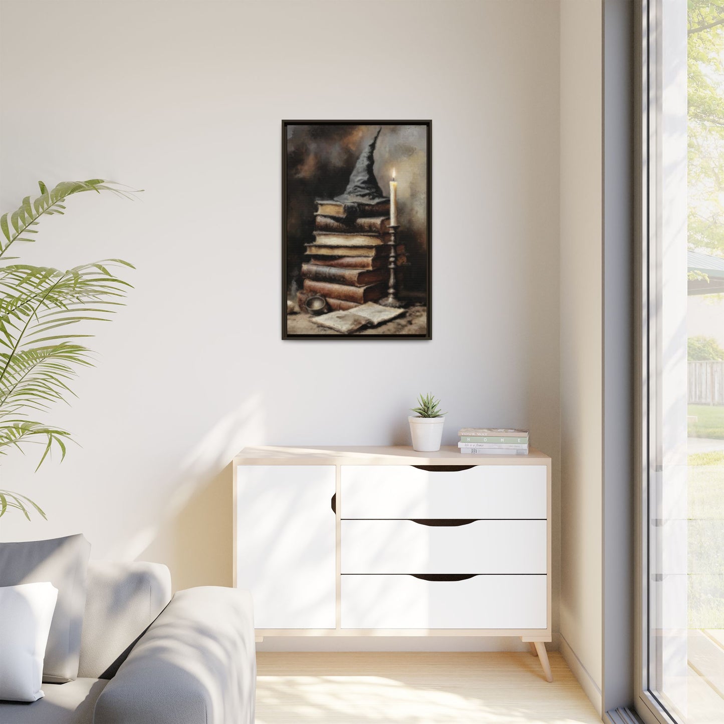 Framed artwork on a wall above a white dresser with a plant and window in the background