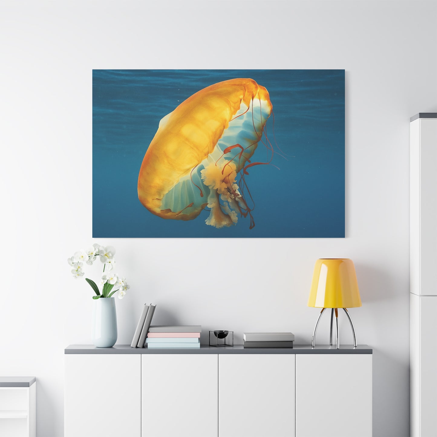 Jellyfish painting on a wall above a white cabinet with a yellow lamp and plant.