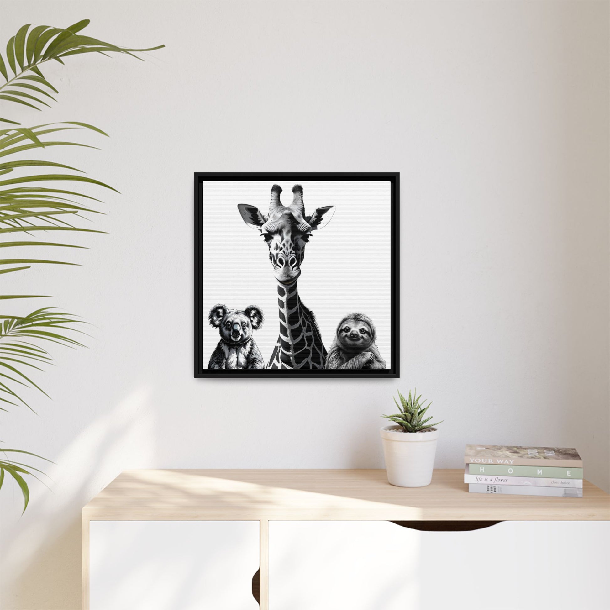 Framed artwork of a giraffe, koala, and sloth on a wall above a desk with a plant and books.