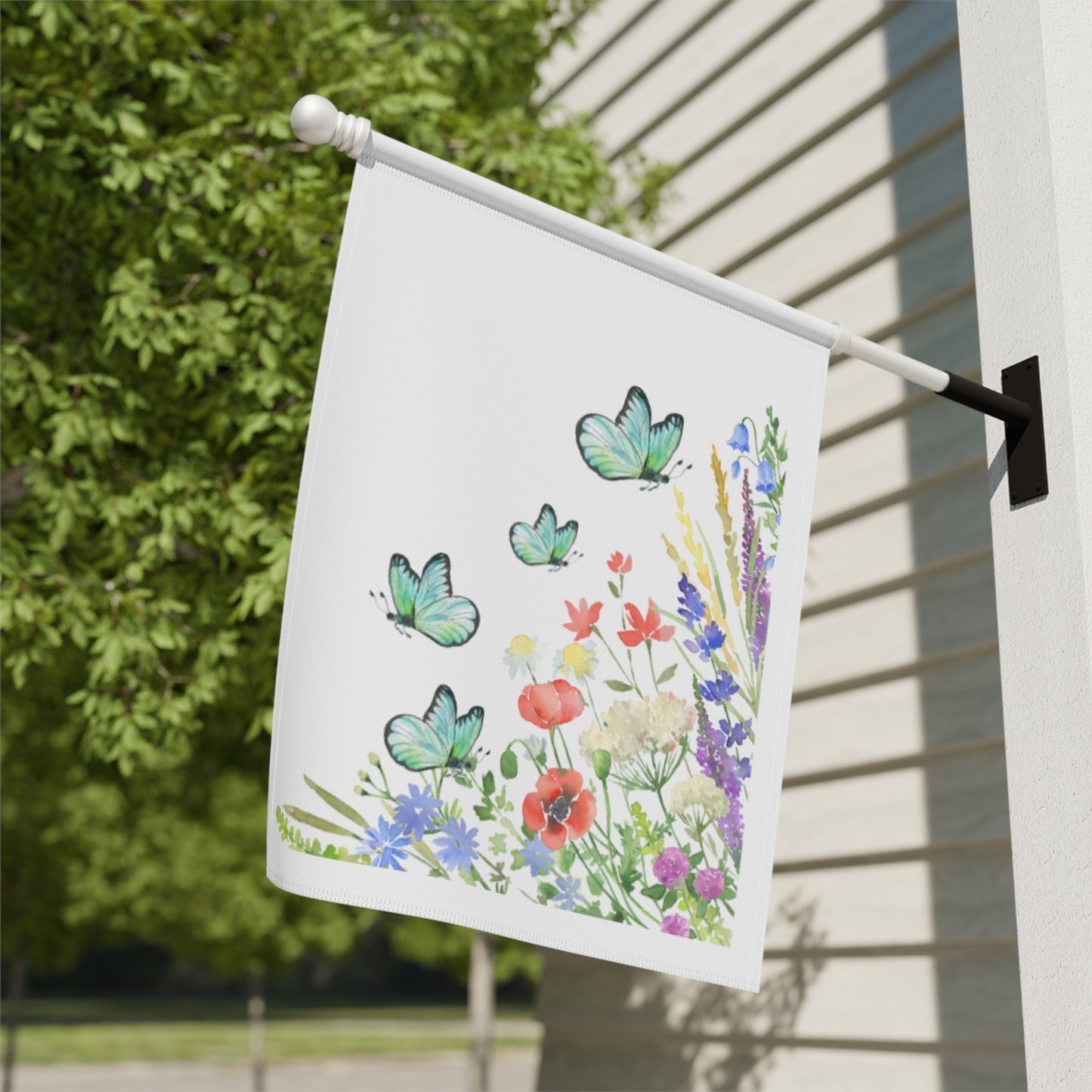 Decorative garden flag with butterflies and flowers on a pole against a house exterior.