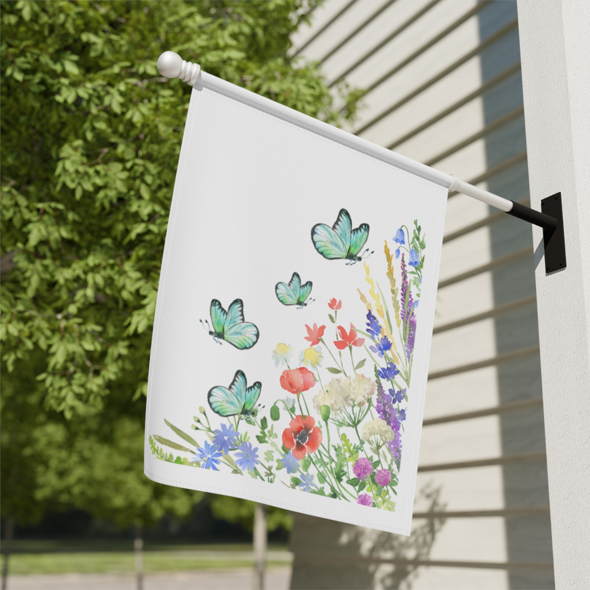 Decorative garden flag with butterflies and flowers on a pole against a house exterior.