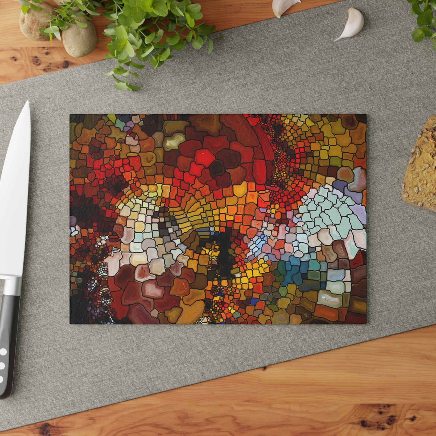 Colorful mosaic art piece on a gray surface with a knife and plant in the background.