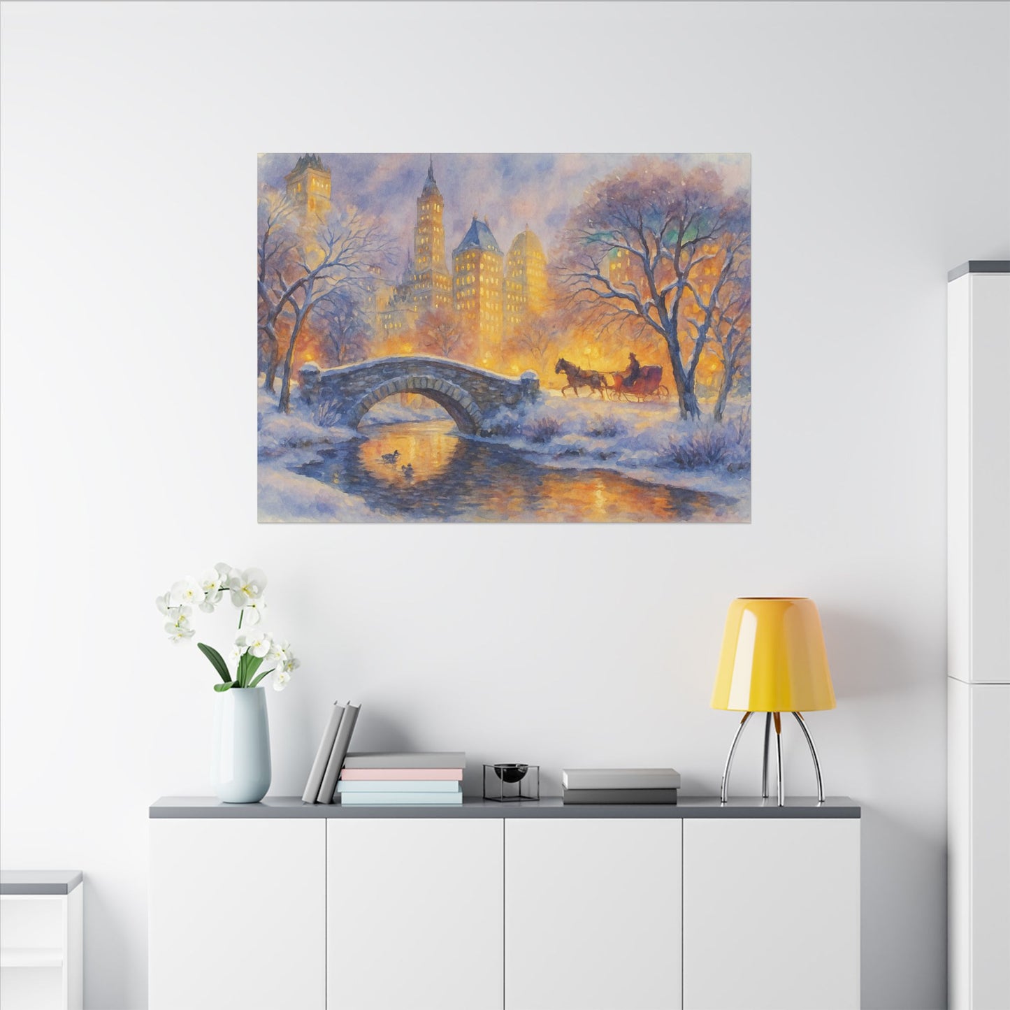 Winter scene with a horse and carriage crossing a bridge over a lake, framed on a wall above a white cabinet.