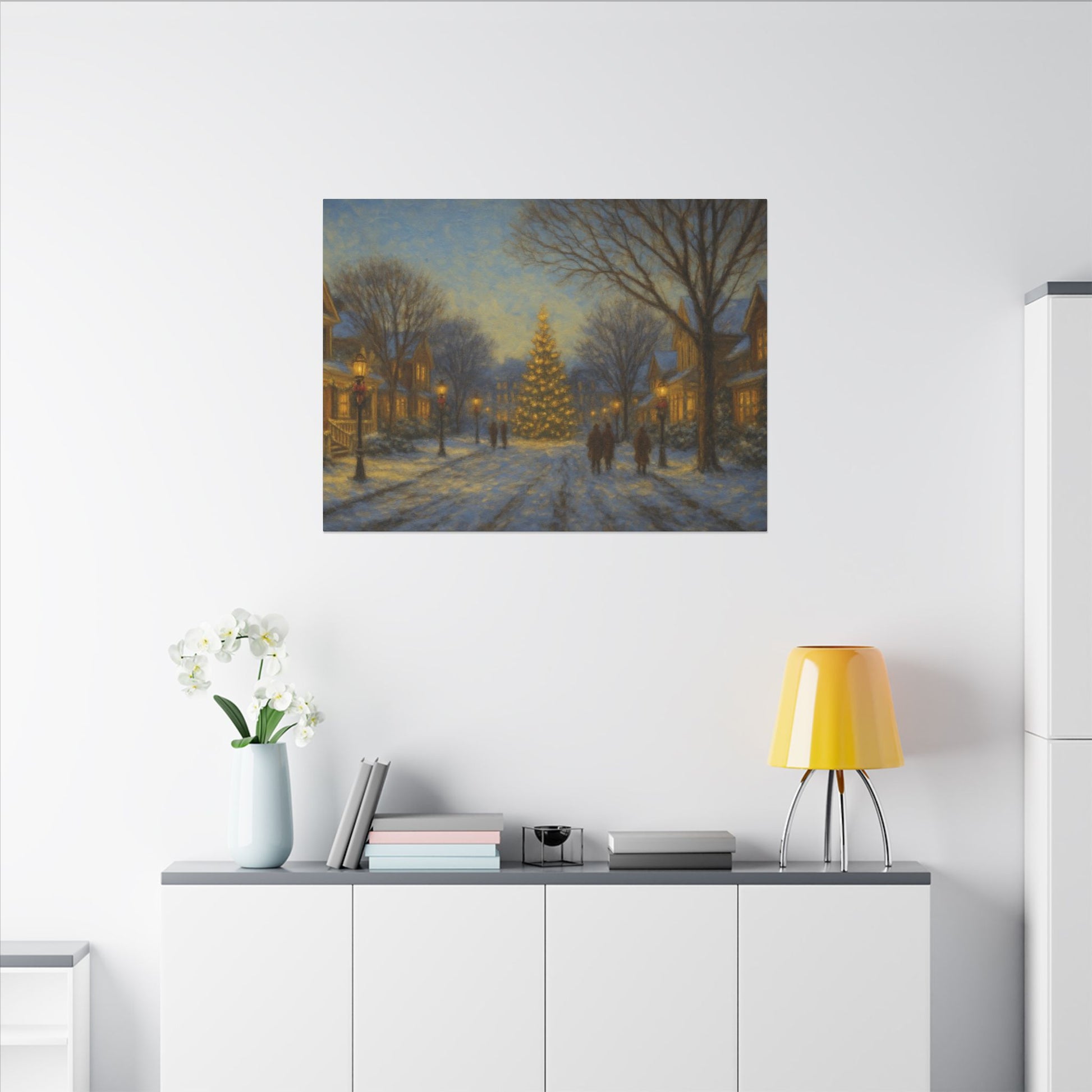 Framed artwork of a snowy street scene with a Christmas tree on a white wall above a shelf.