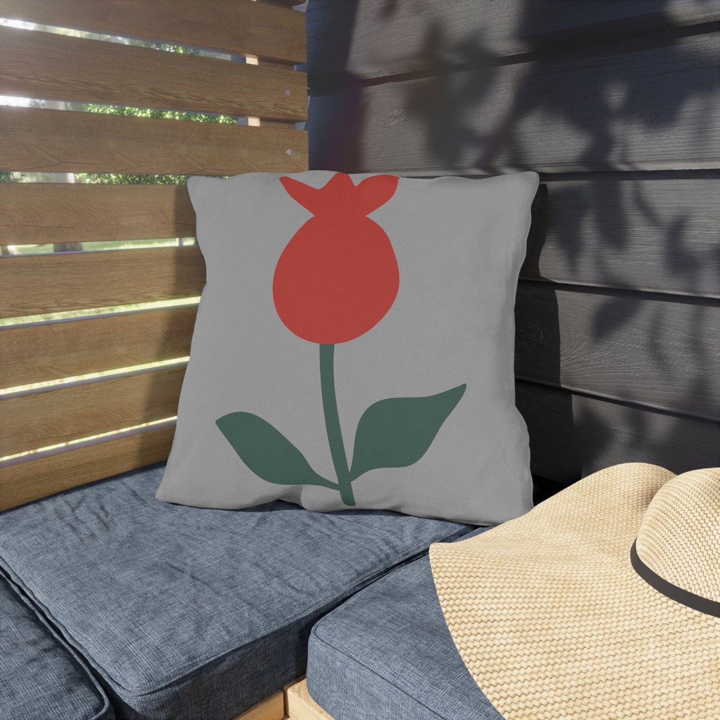 Gray pillow with a red flower design on a wooden bench
