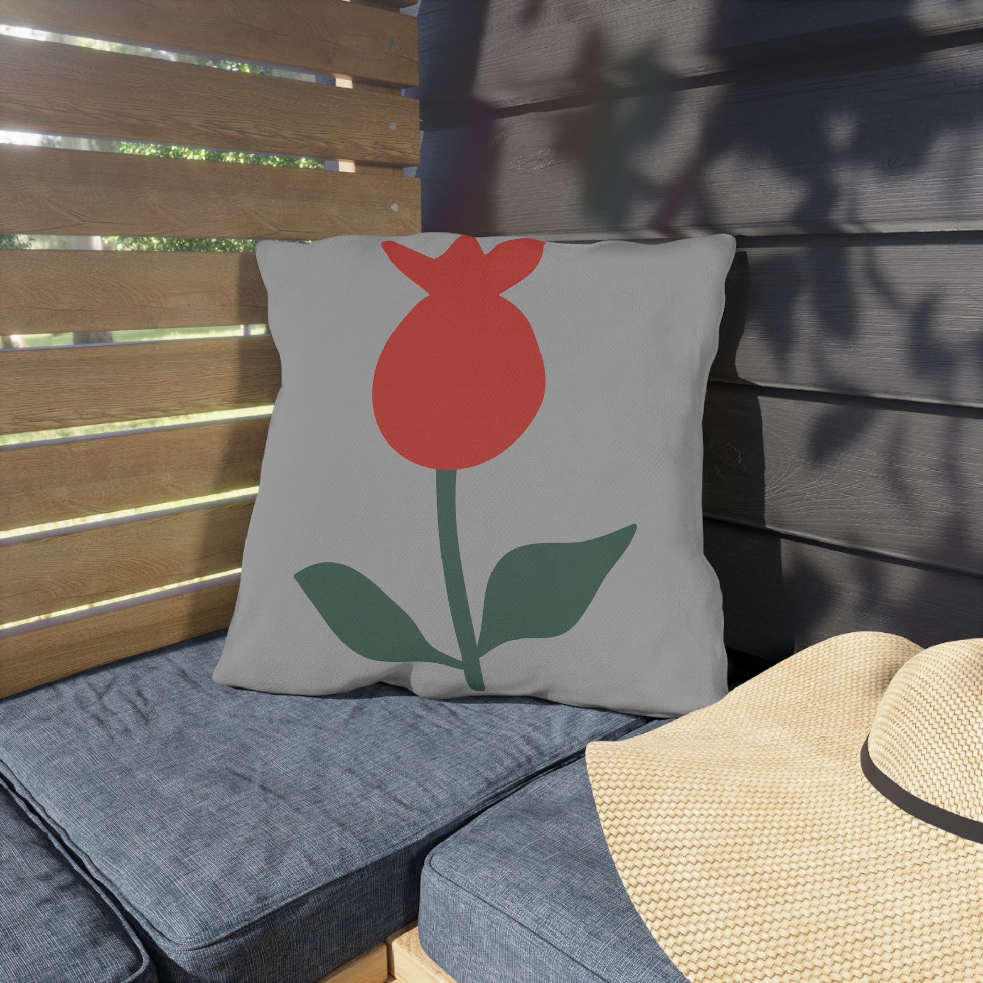 Gray pillow with a red flower design on a wooden bench