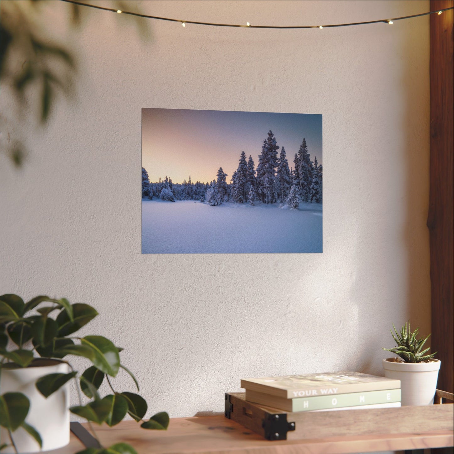 Framed photograph of a snowy forest on a wall above a wooden desk with plants.