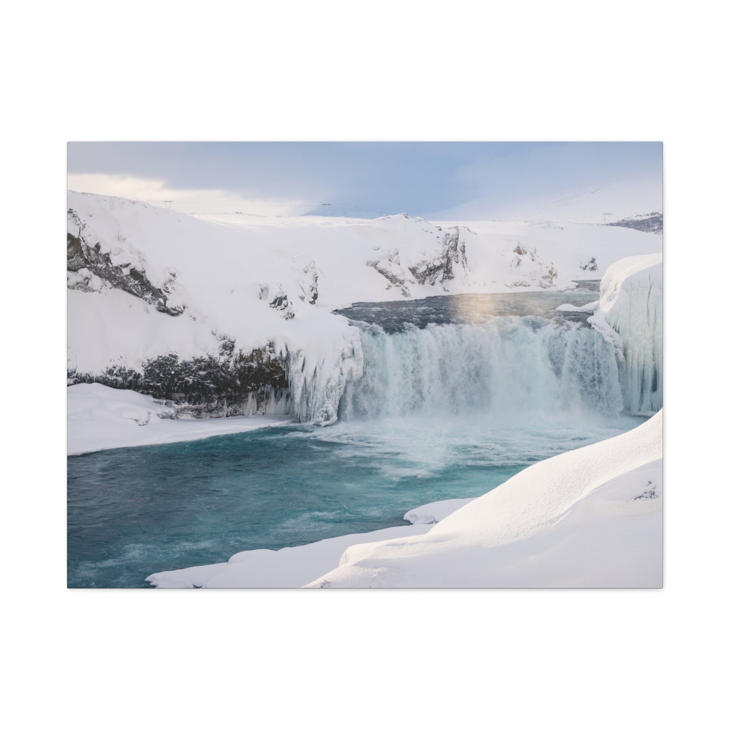 Frozen waterfall in a snowy landscape with a clear blue sky.