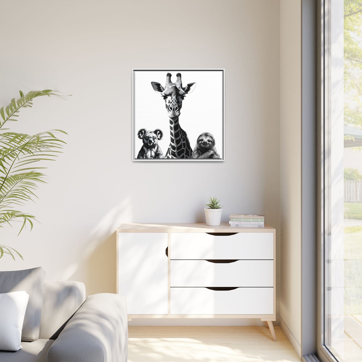 Framed artwork of a giraffe with two sloths on a wall above a white cabinet.