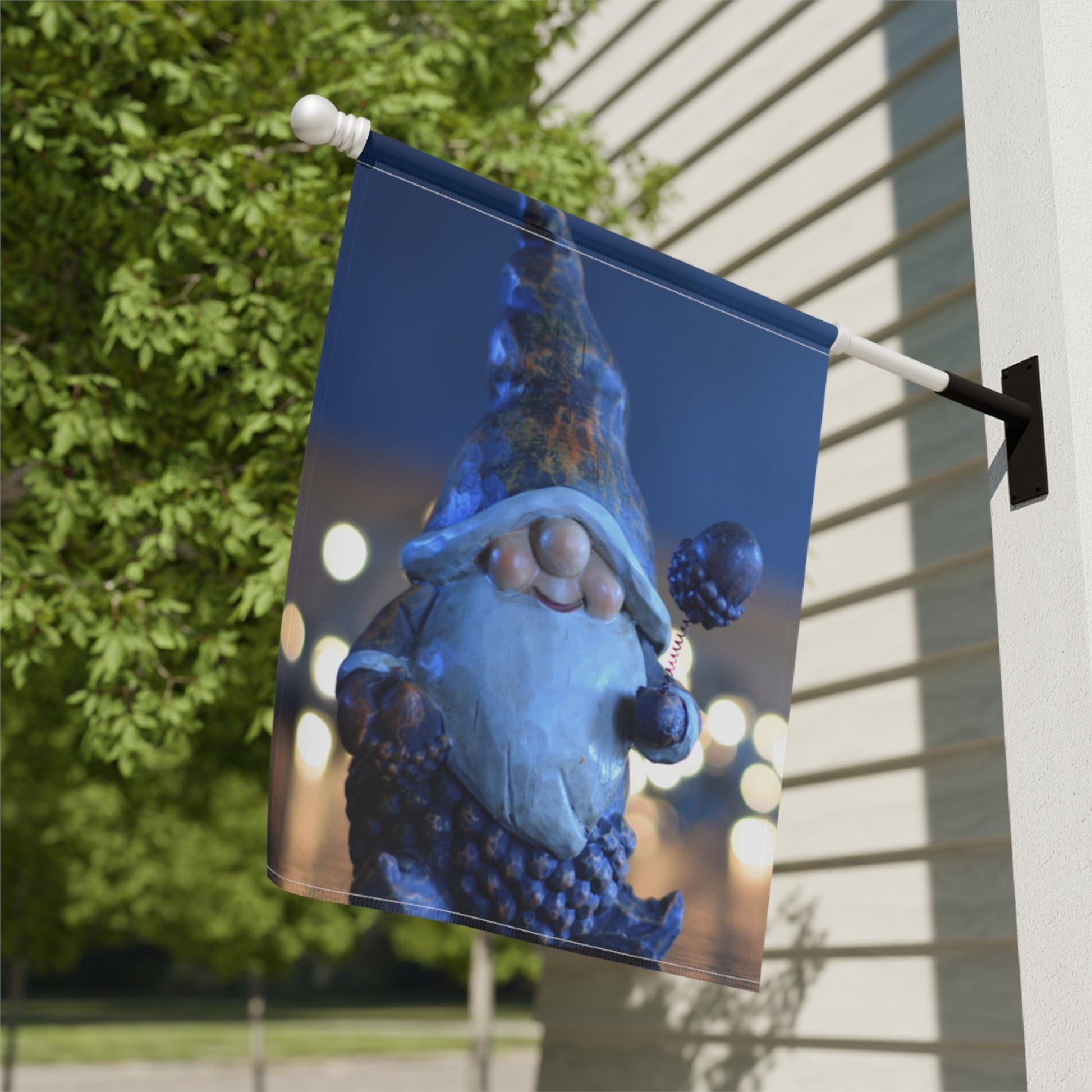 Decorative garden flag with a gnome design on a pole against a building and tree background.