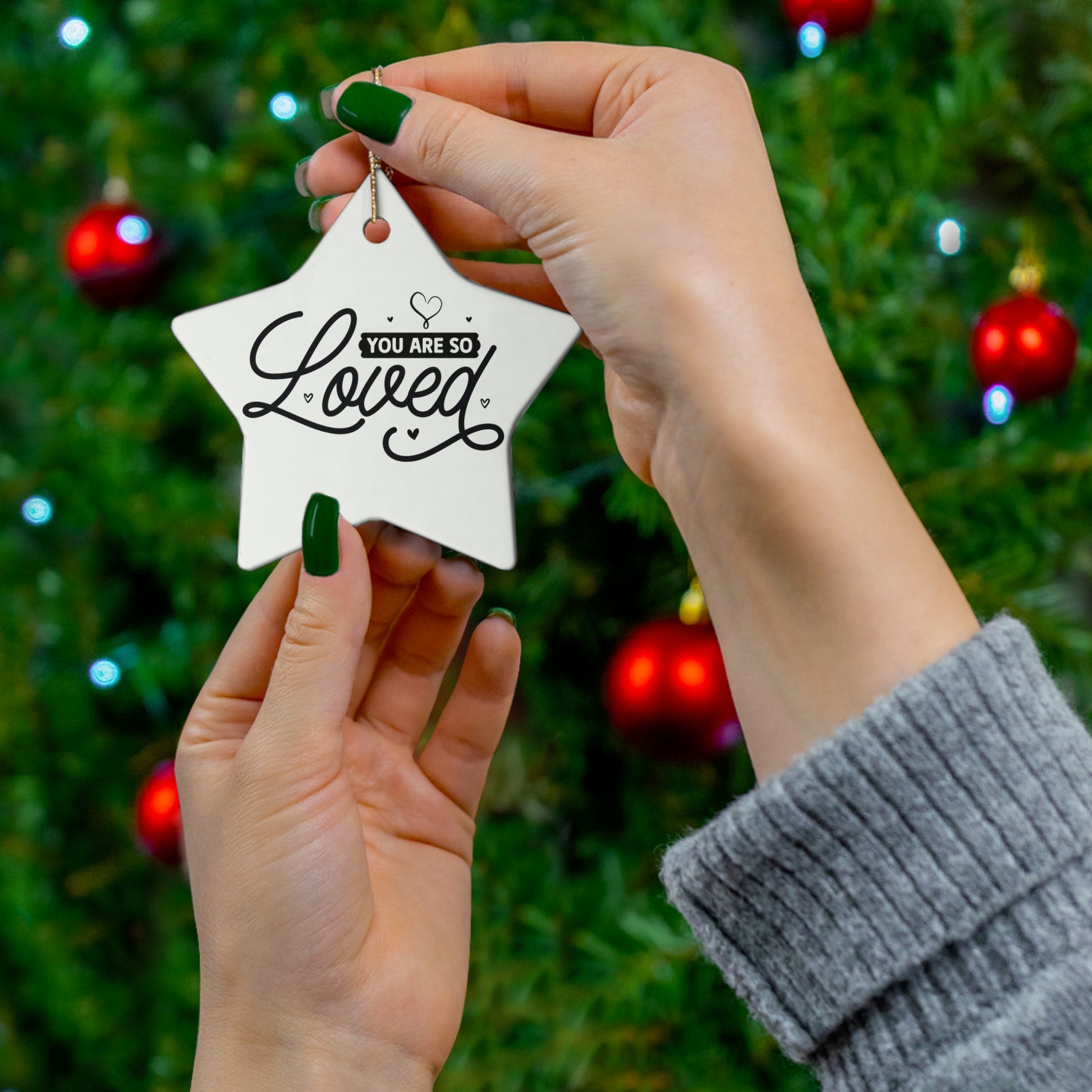 Star-shaped ornament with 'You are so loved' text held by hands against a Christmas tree background