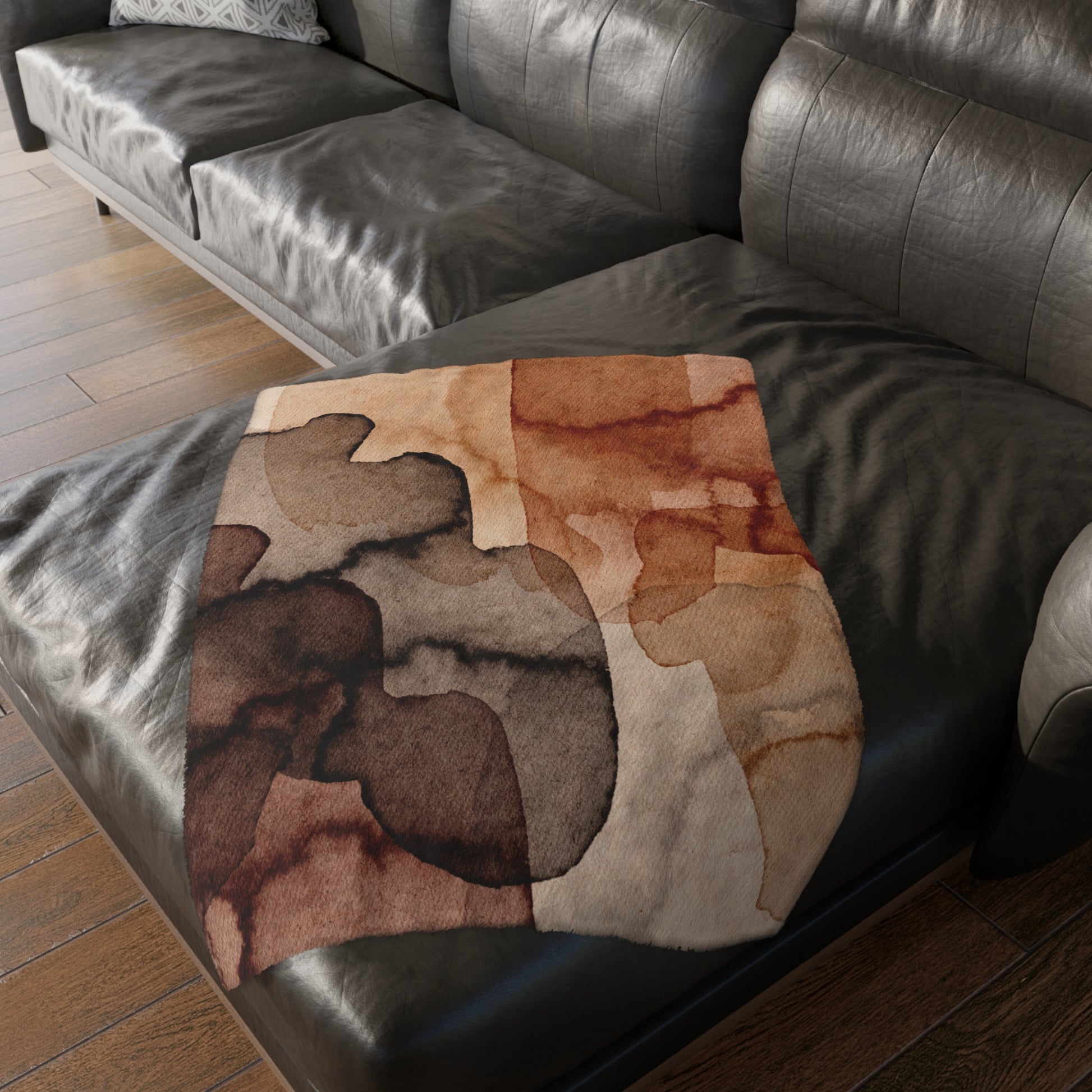 Brown patterned blanket on a dark leather sofa with wooden floor.