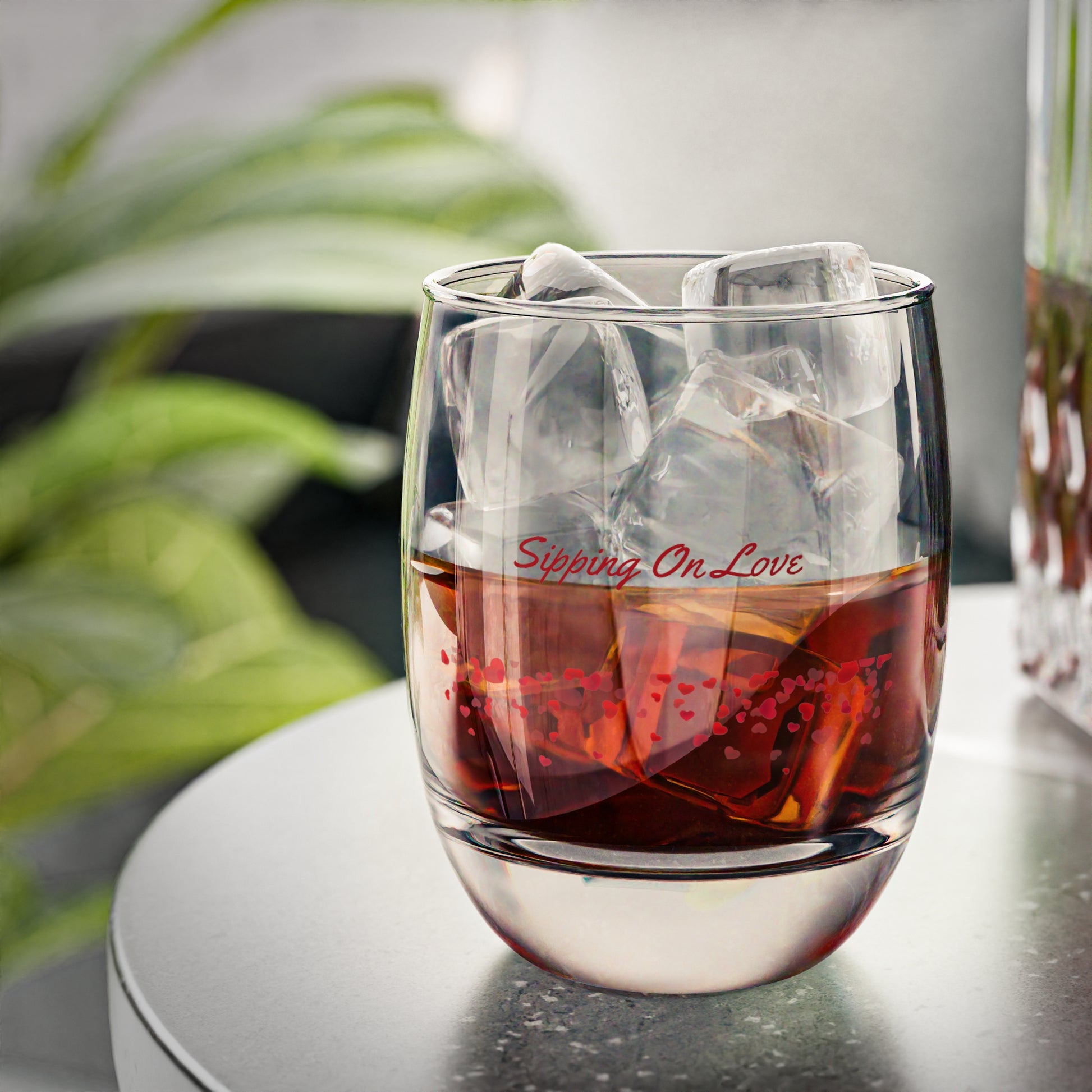 Glass of red liquid with ice cubes and 'Sipping On Love' text on a blurred background