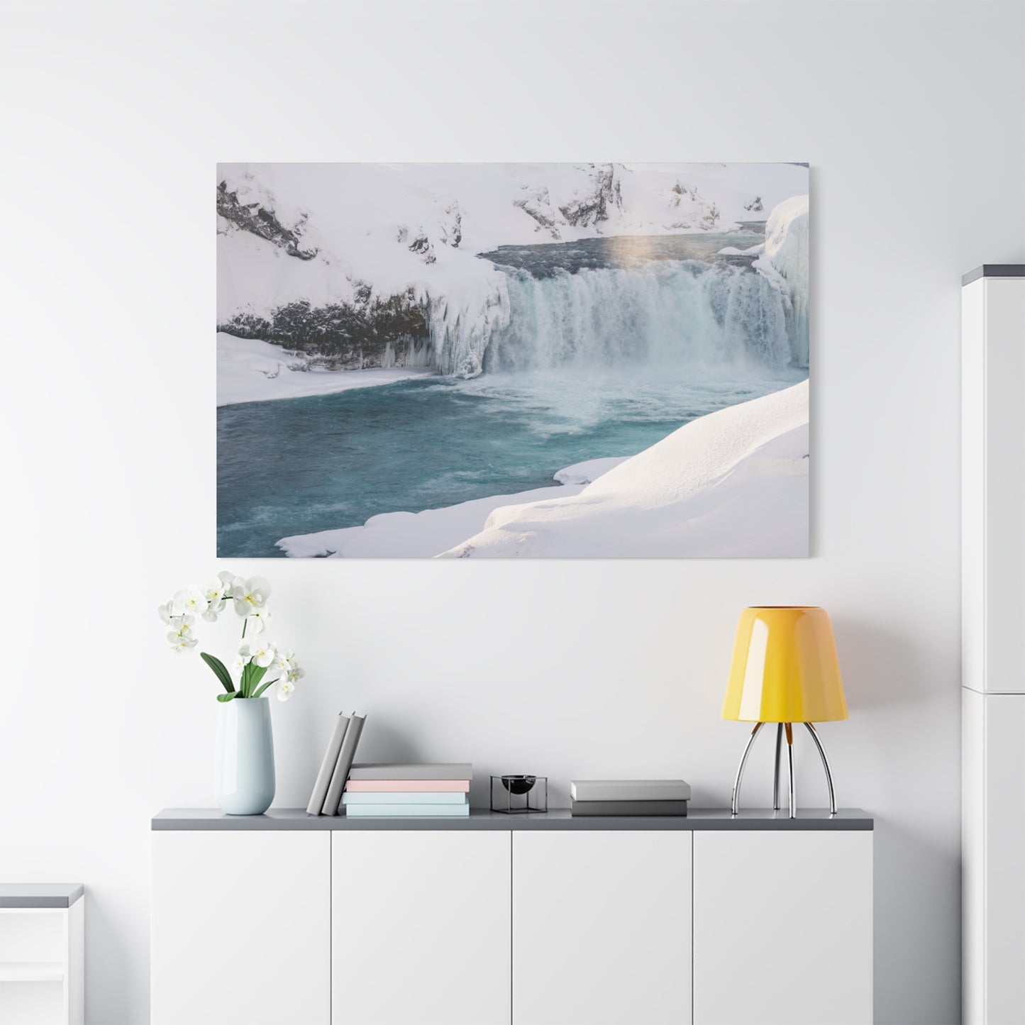 Framed photograph of a snowy landscape with a waterfall hanging on a white wall above a desk.