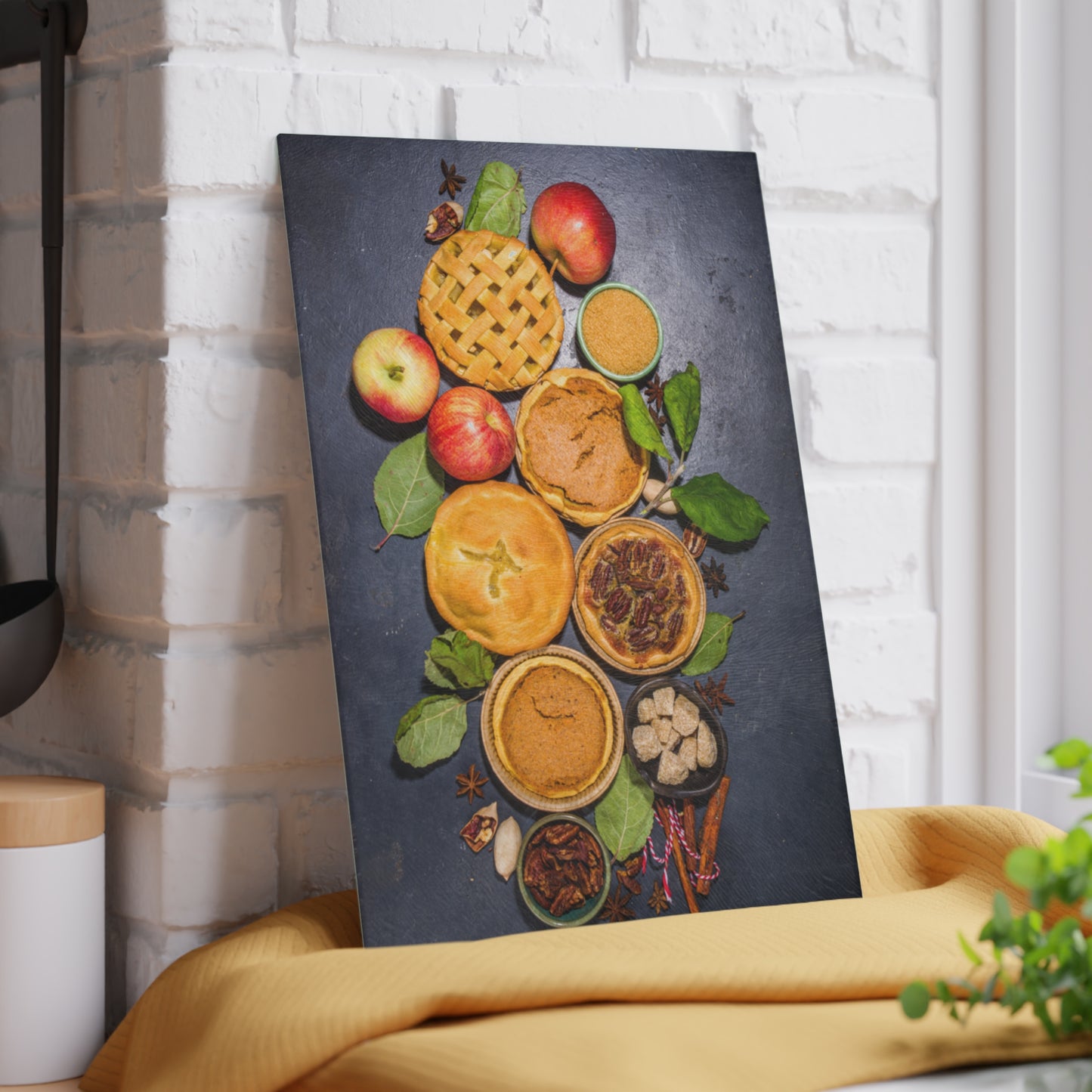 Canvas print of pies and apples on a dark background, leaning against a white brick wall.
